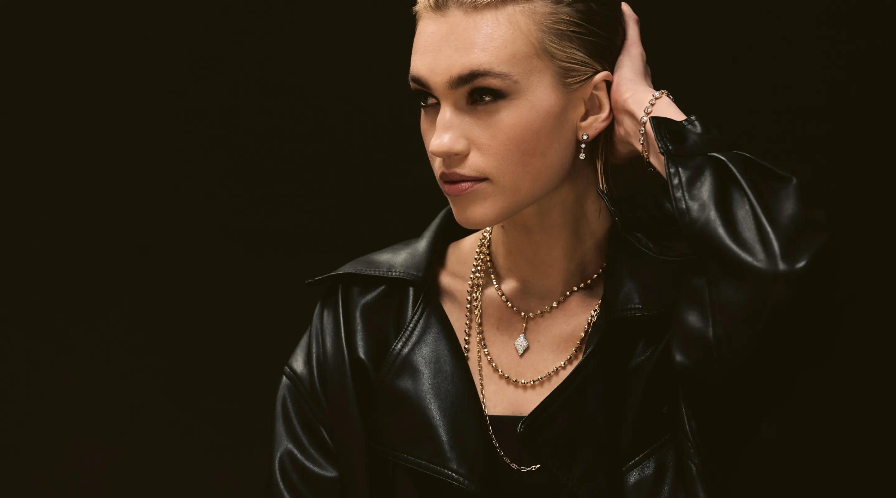 Blonde woman with slicked-back hair wearing a black strapless top and a choker necklace with a large light blue gemstone.