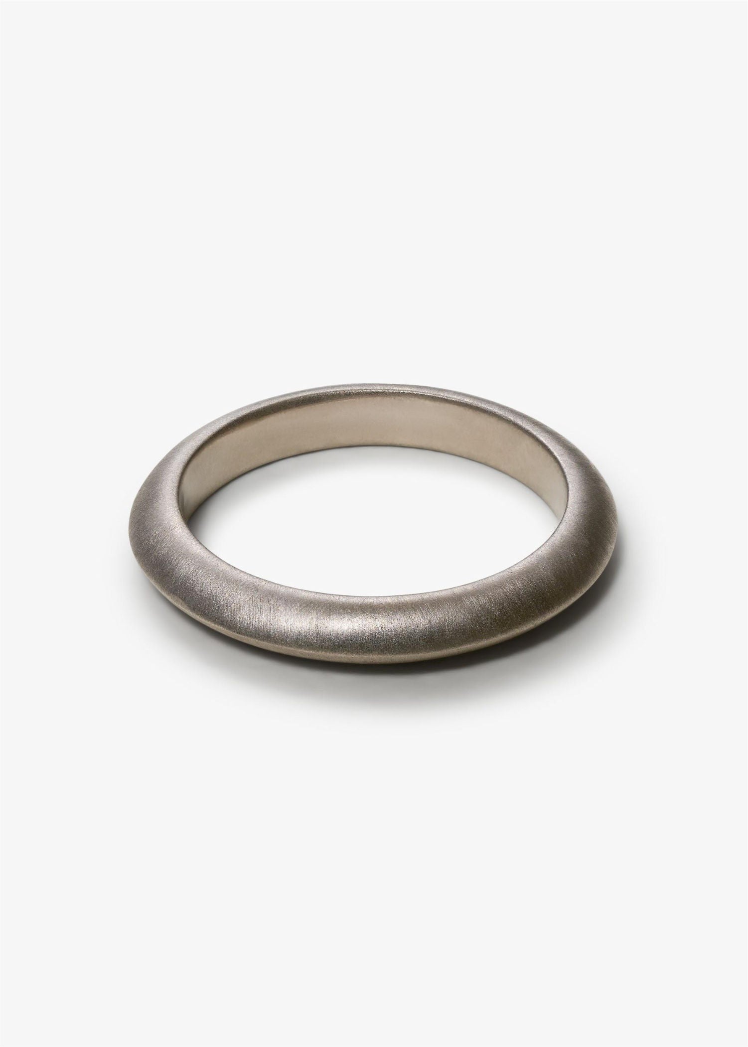 Simple white gold knife-edge ring on a textured gray surface.