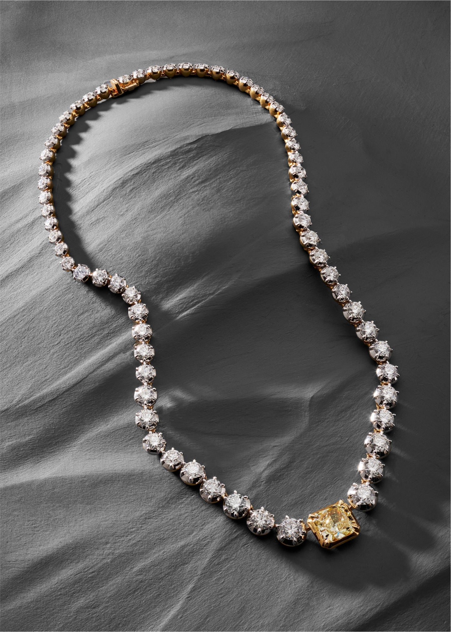 lose-up of a model wearing a gold diamond necklace featuring a large yellow diamond centerpiece surrounded by round white diamonds.