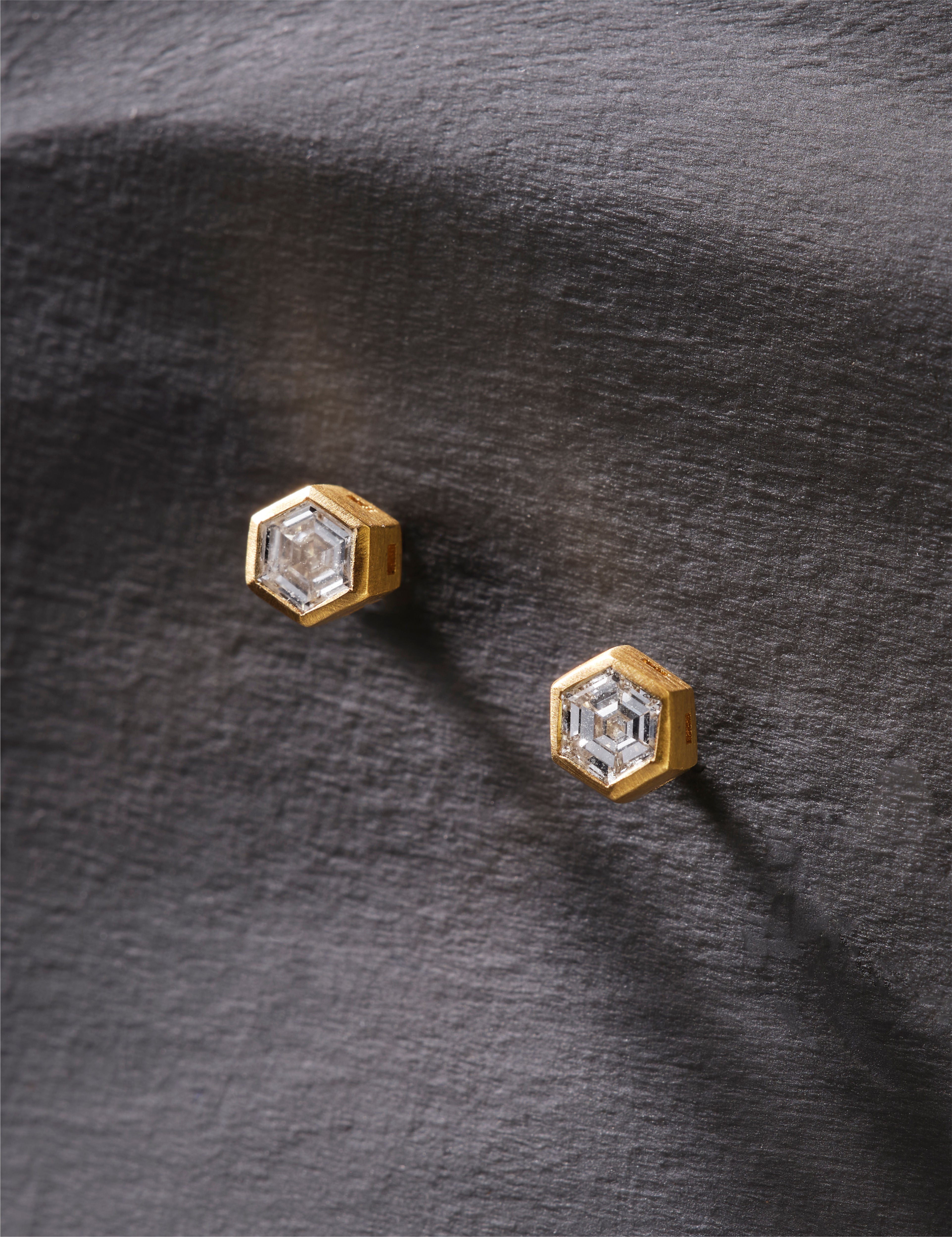 Hexagonal earrings with gold and white design on a light gray background.