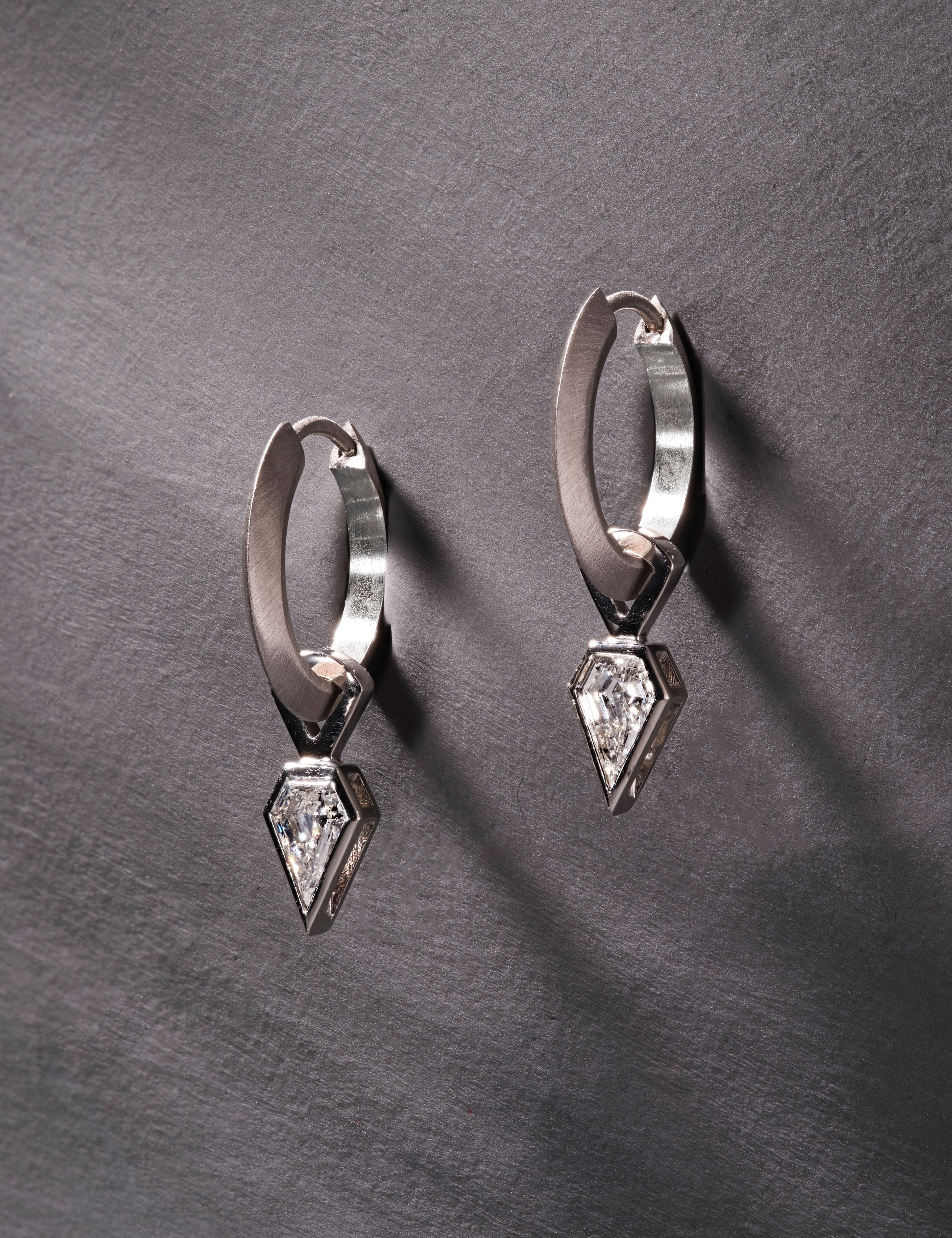 Platinum hoop earrings featuring shield-cut diamonds on grey textured background.