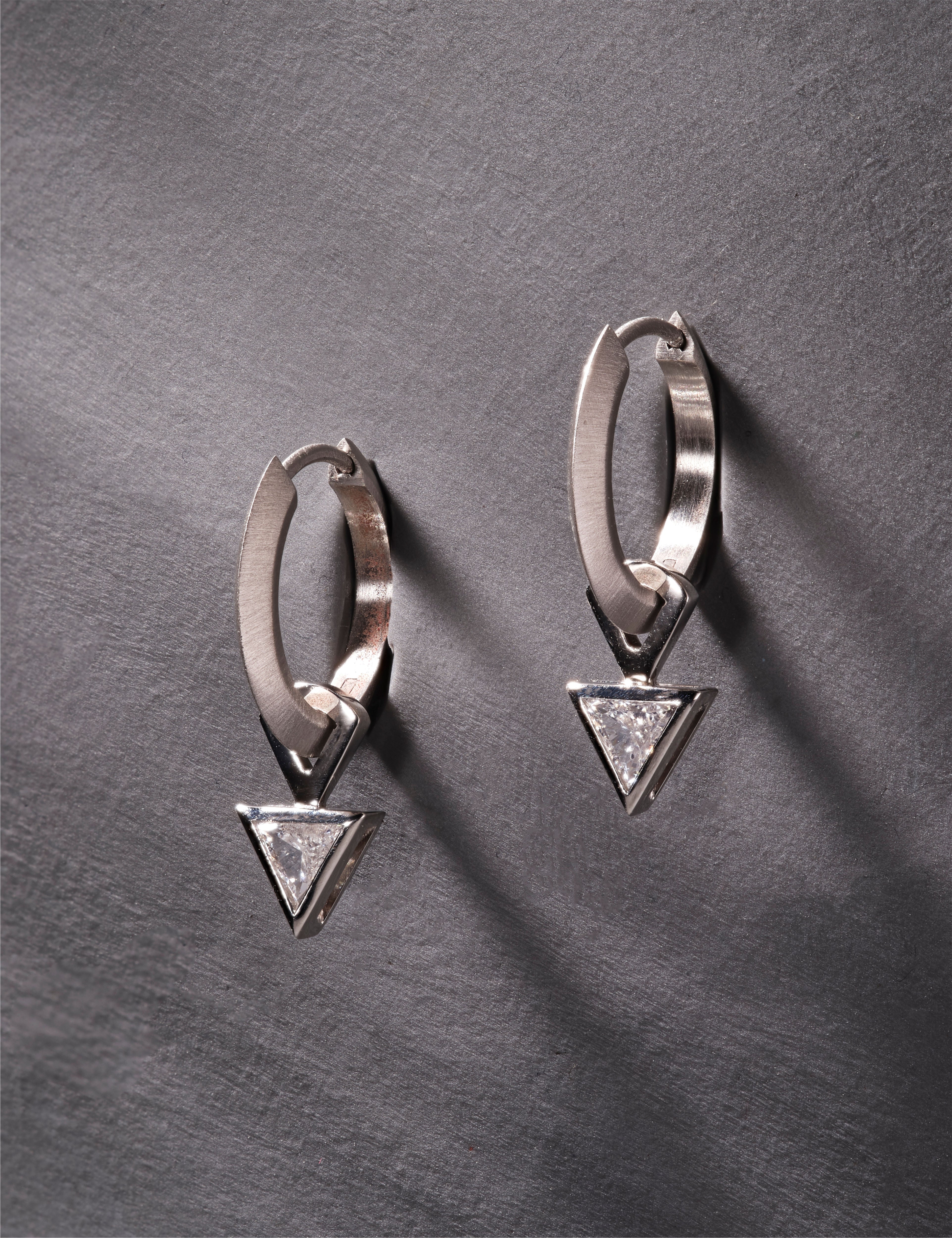 Platinum hoop earrings featuring triangular-cut diamonds on grey textured background.