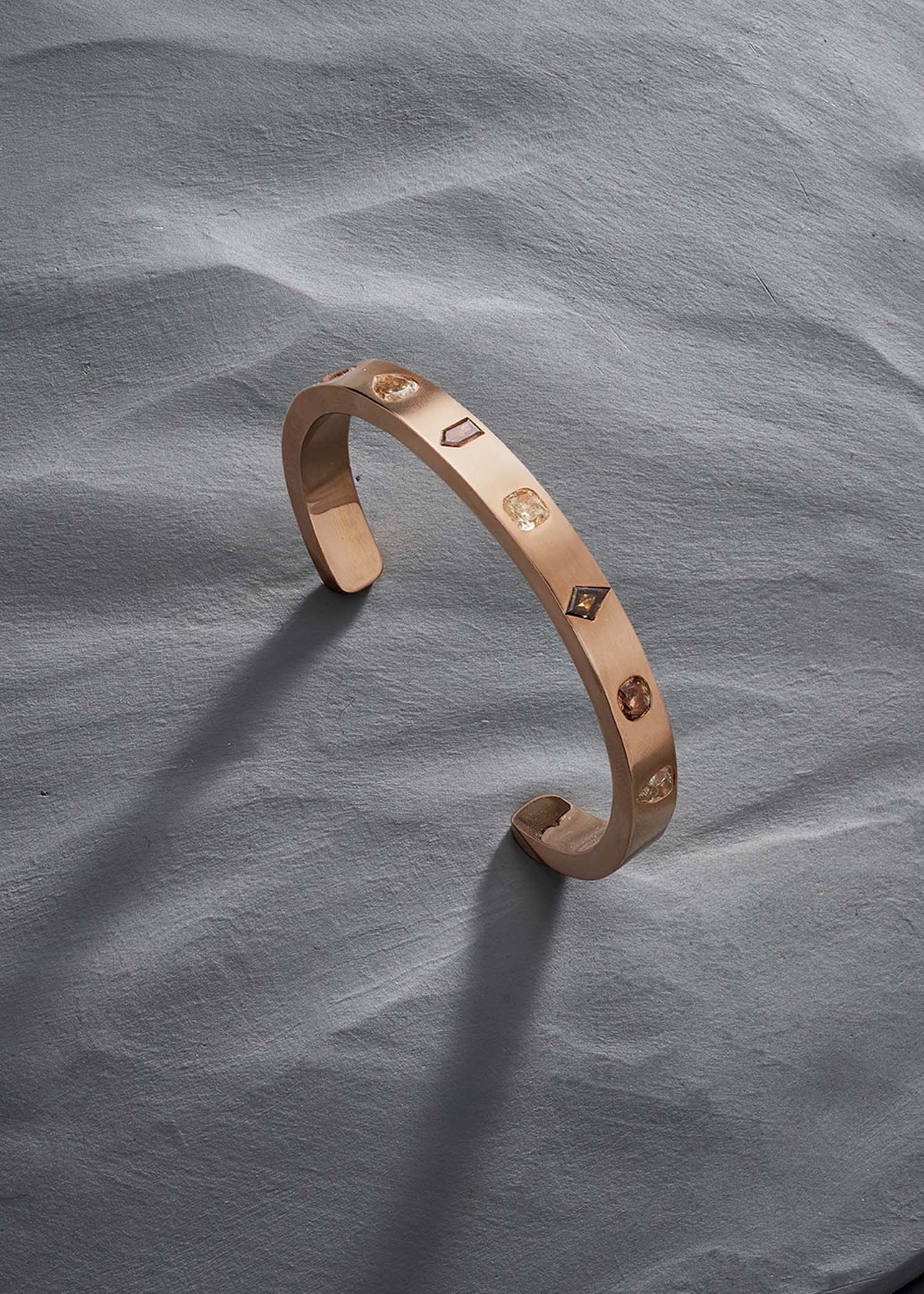 Rose gold diamond cuff bracelet with geometric gems on a textured gray surface.