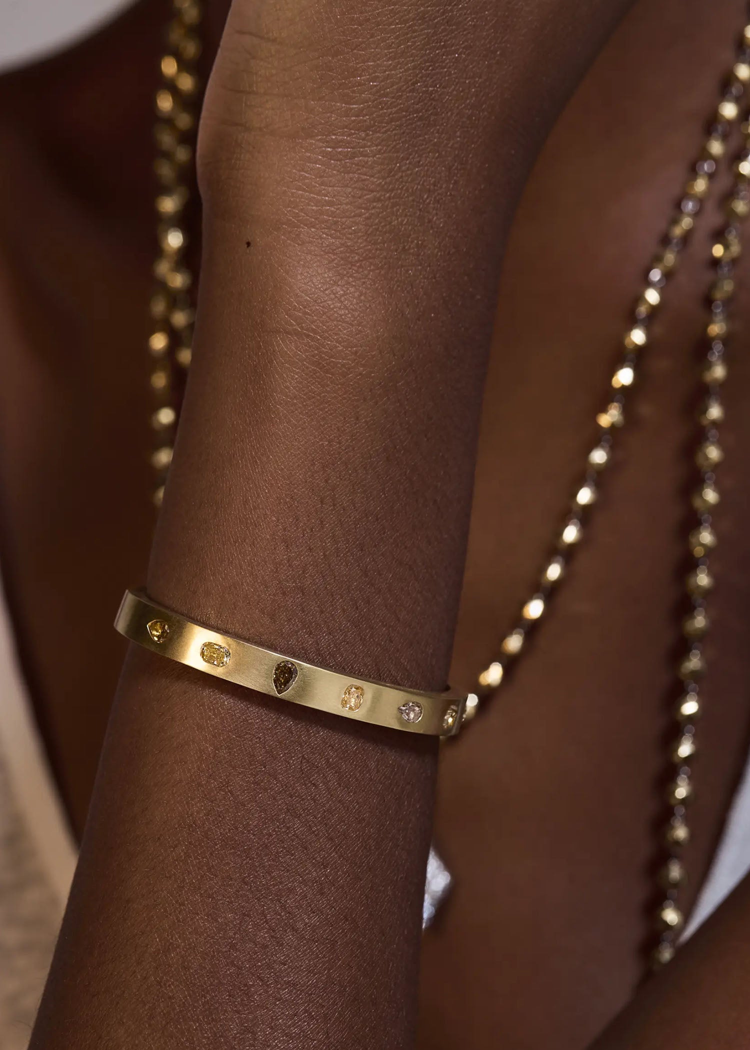 Yellow gold diamond cuff bracelet with geometric gems on a textured gray surface.