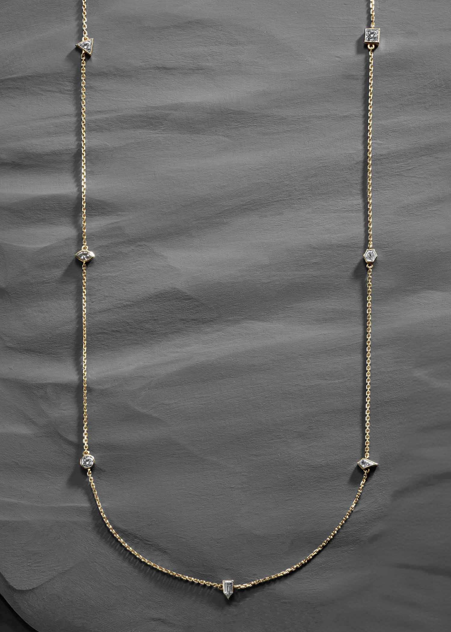 Elegant long gold chain necklace featuring bezel-set diamonds in various cuts, including round, square, and triangular shapes, displayed on a white background.