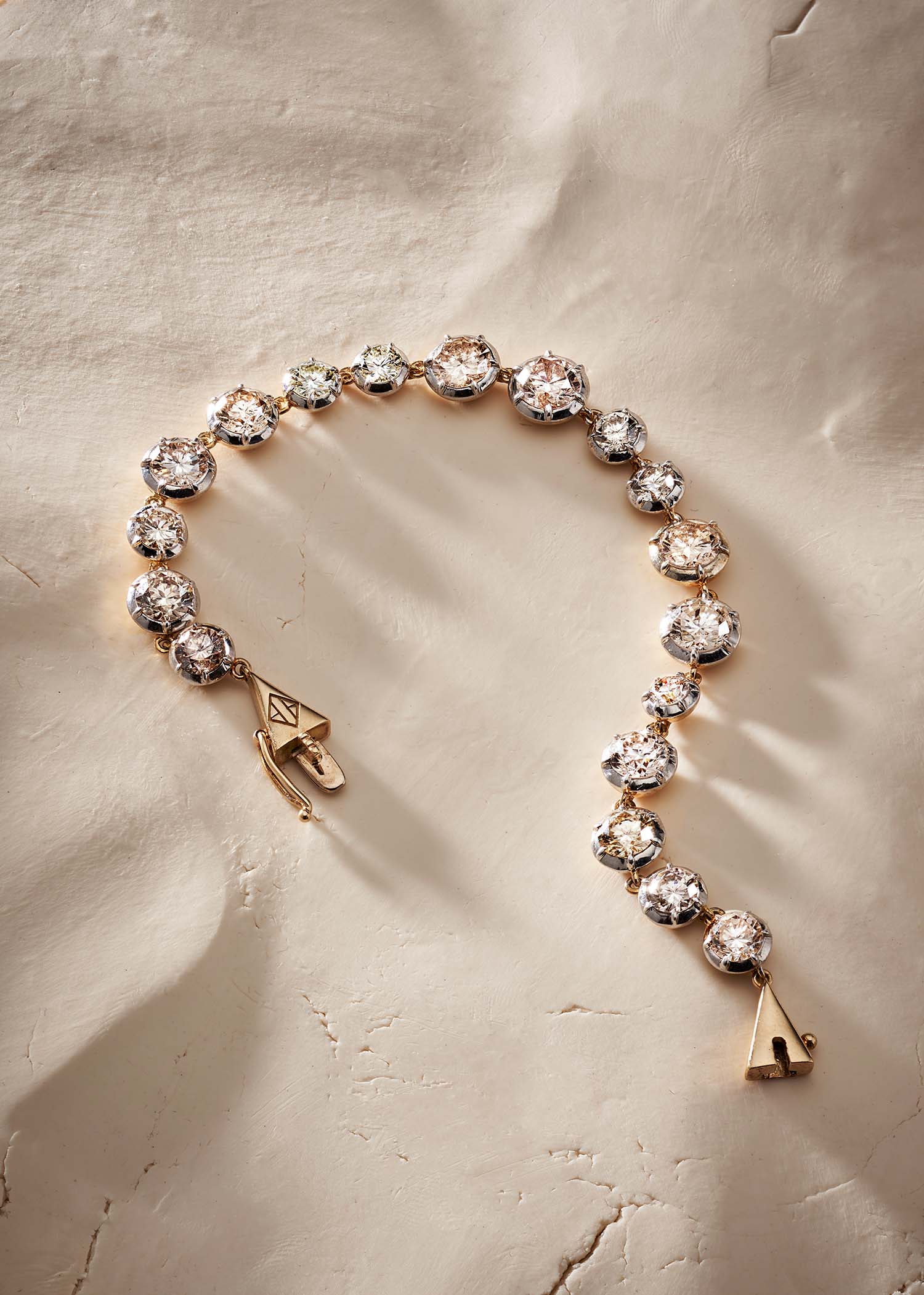 Gold diamond tennis bracelet with round-cut diamonds displayed on a soft beige textured surface.