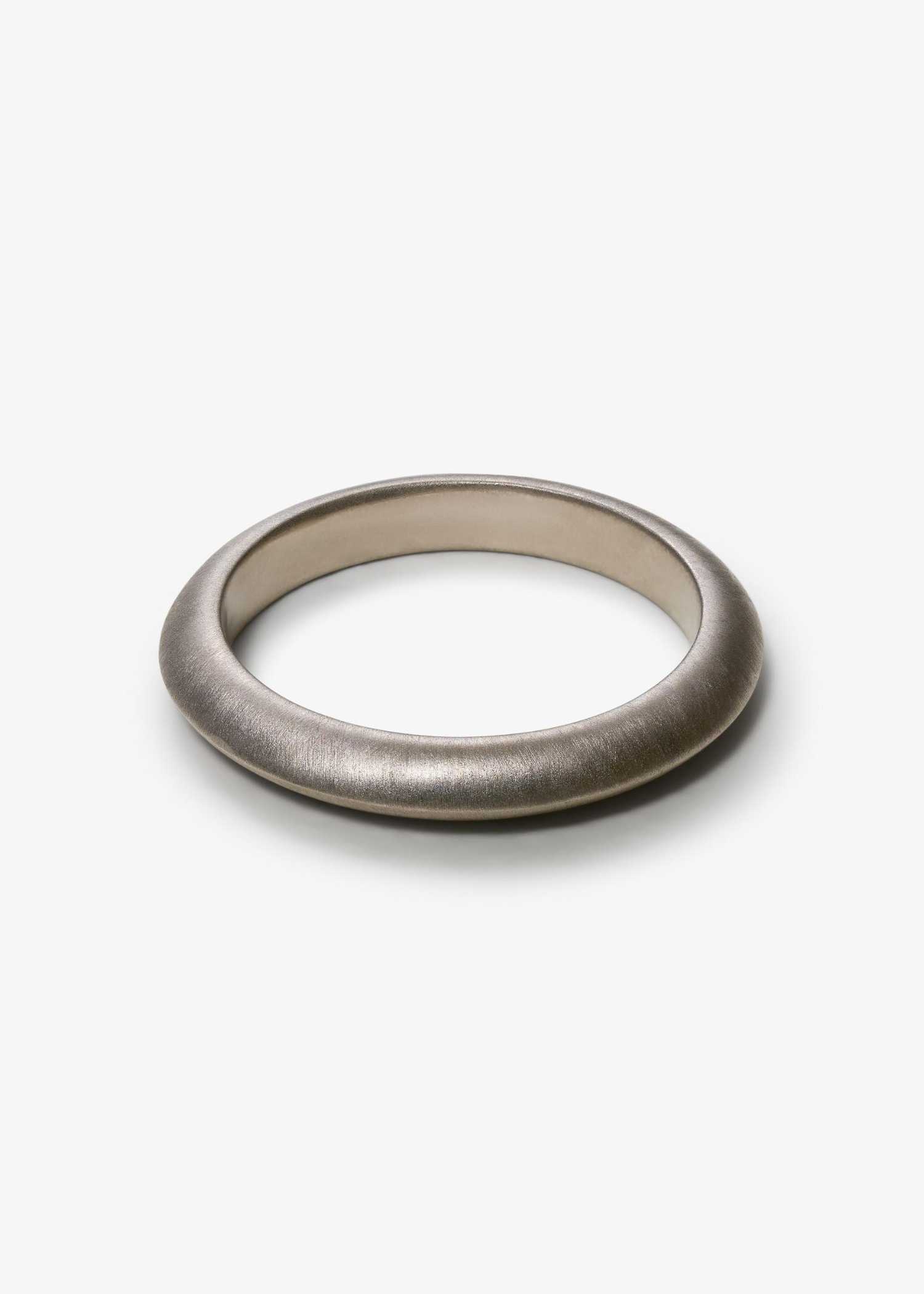 Simple white gold knife-edge ring on a textured gray surface.