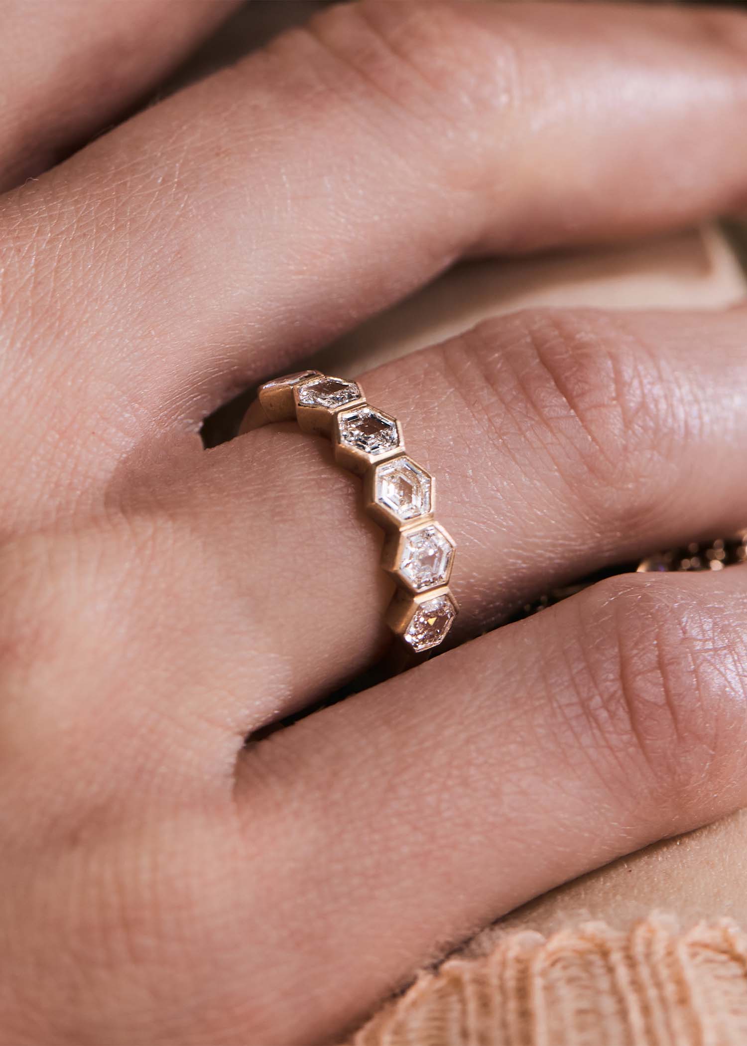Close-up of a gold hexagon diamond eternity ring worn on a finger, showing the geometric setting detail.