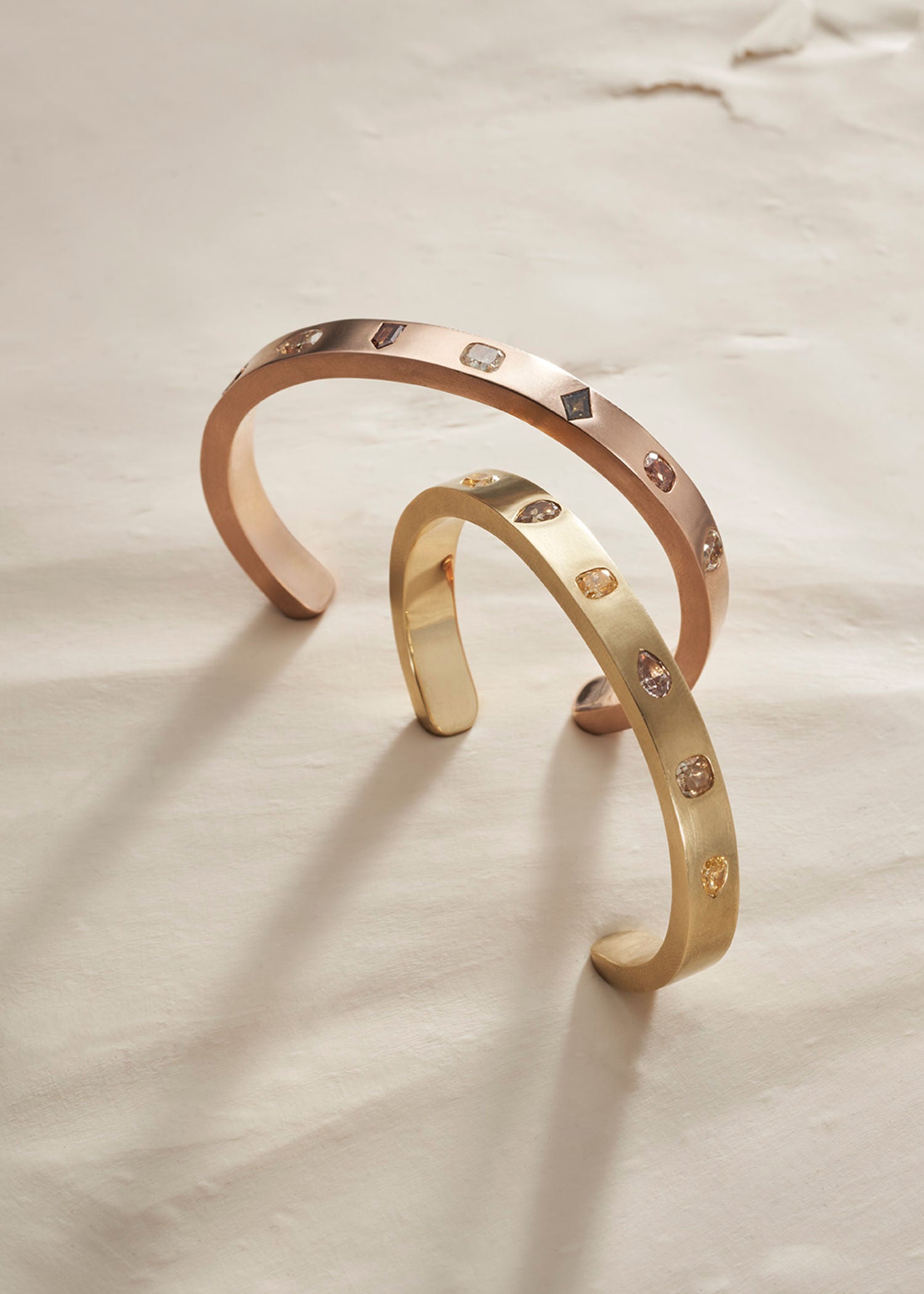Two gold bangles on a light clay background.