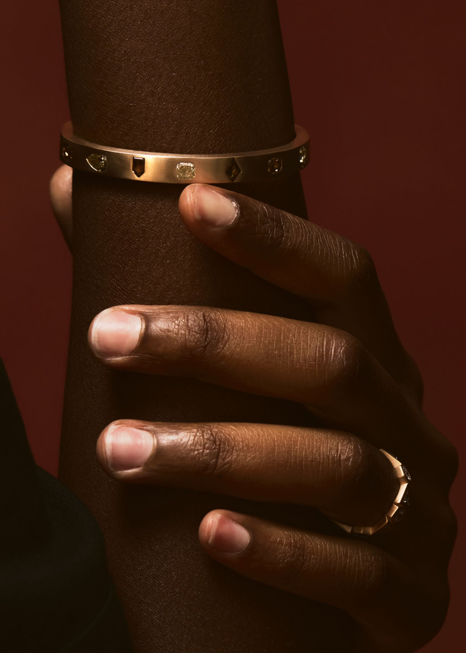 Hand wearing a gold bracelet and ring on a dark background.