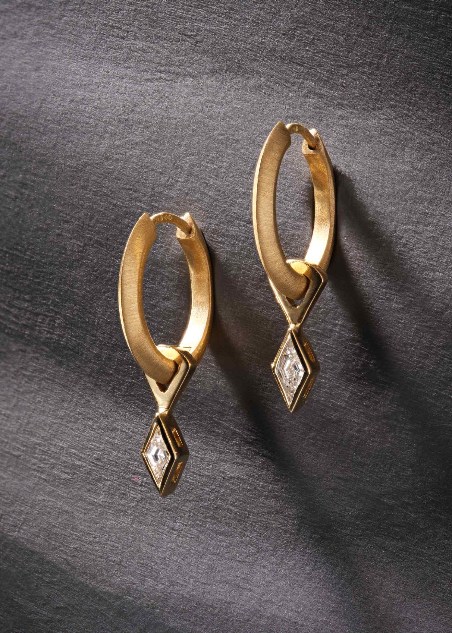 Yellow gold hoop earrings featuring lozenge-cut diamonds on grey textured background.
