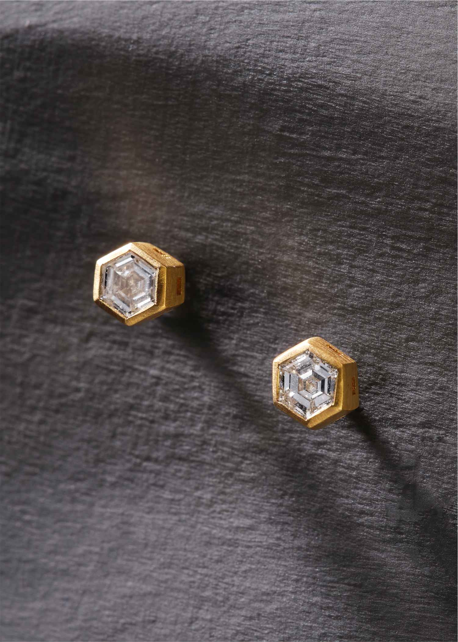 Hexagonal earrings with gold and white design on a light gray background.
