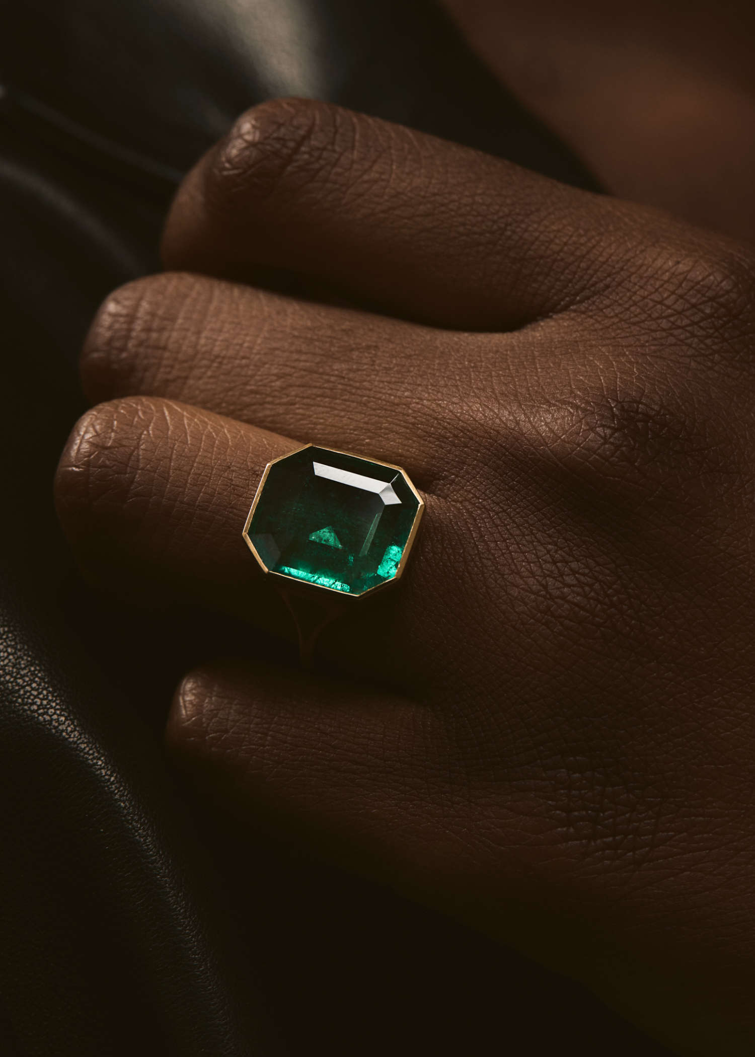 Yellow gold ring set with a large hexagonal green emerald on a textured beige surface.