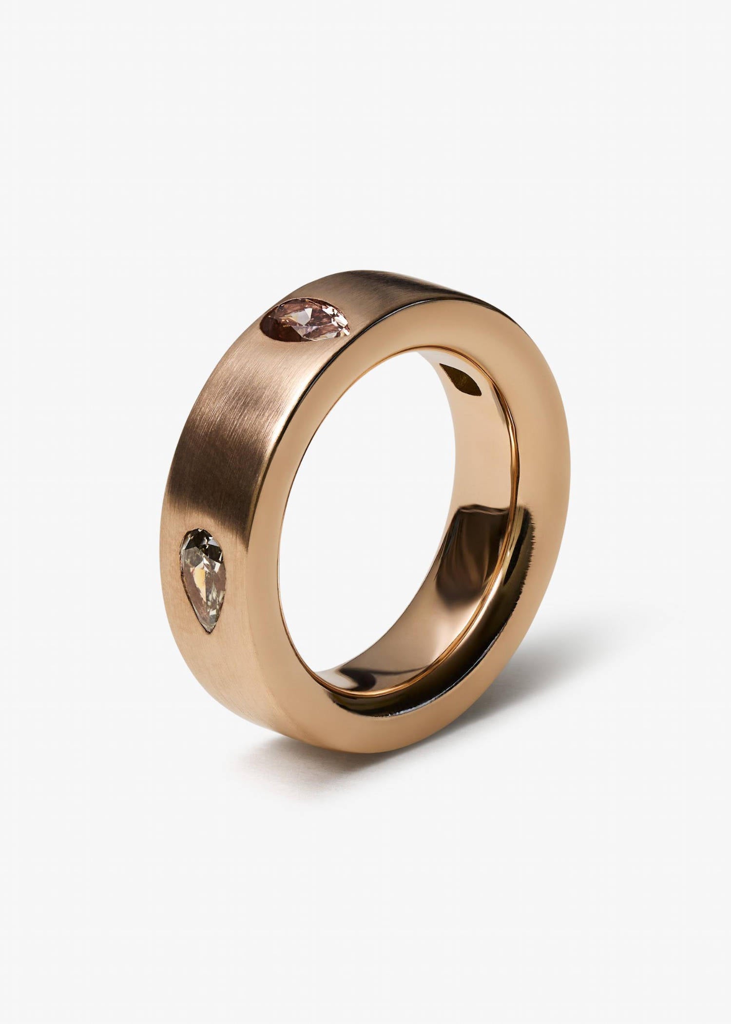 Rose gold ring with pear-cut diamonds on matte textured surface.
