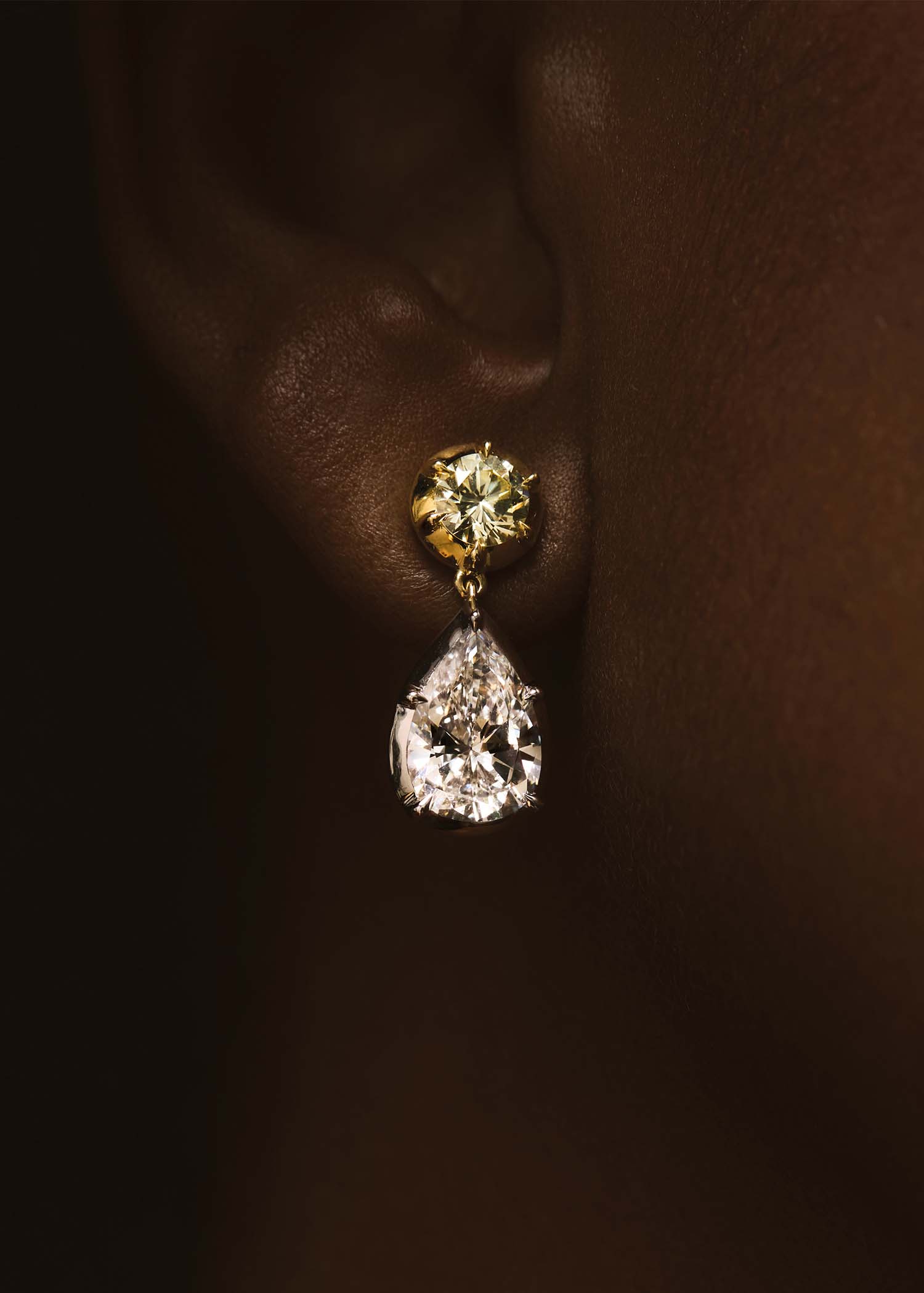 Pair of diamond earrings with gold and silver accents on a textured gray surface.
