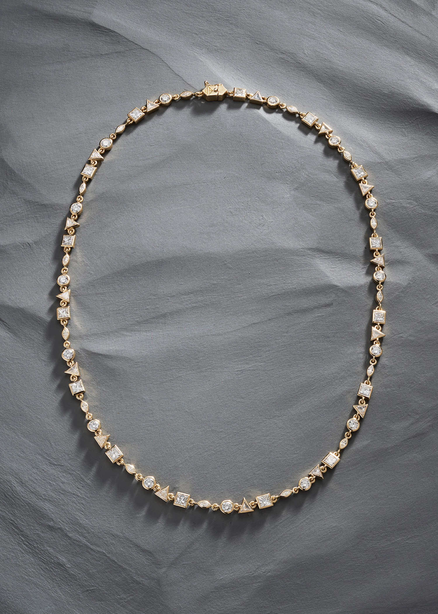 18k yellow gold tennis necklace featuring alternating round, square, marquise, and triangle-cut diamonds on grey background.