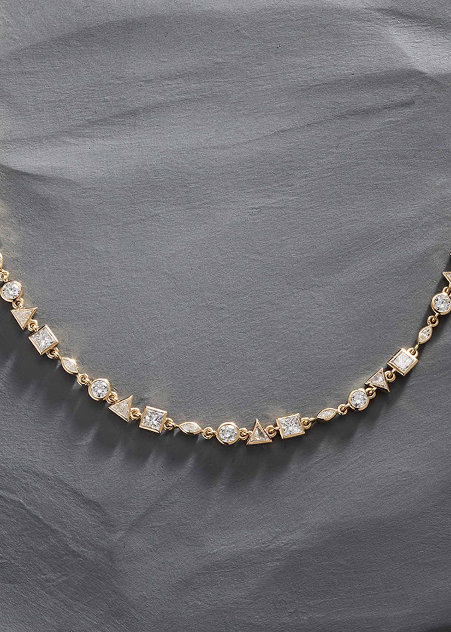 Close-up of yellow gold diamond tennis necklace showcasing geometric diamond cuts including round, square, and triangle shapes.