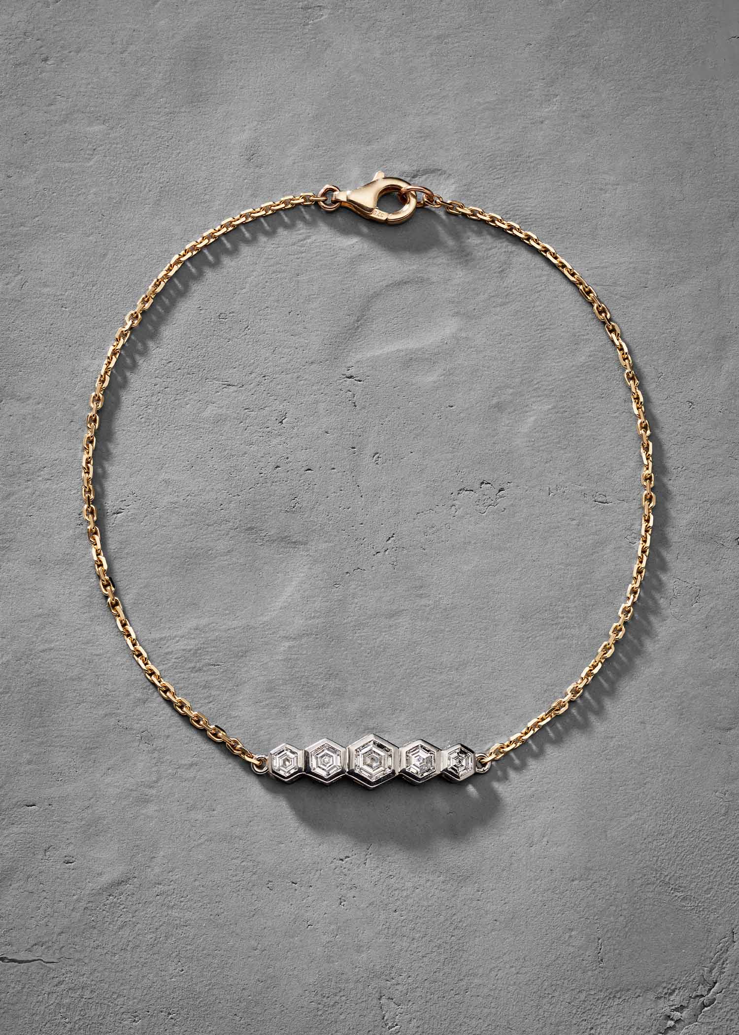 Yellow gold bracelet featuring five hexagon-cut diamonds set in geometric white gold pattern on grey background.