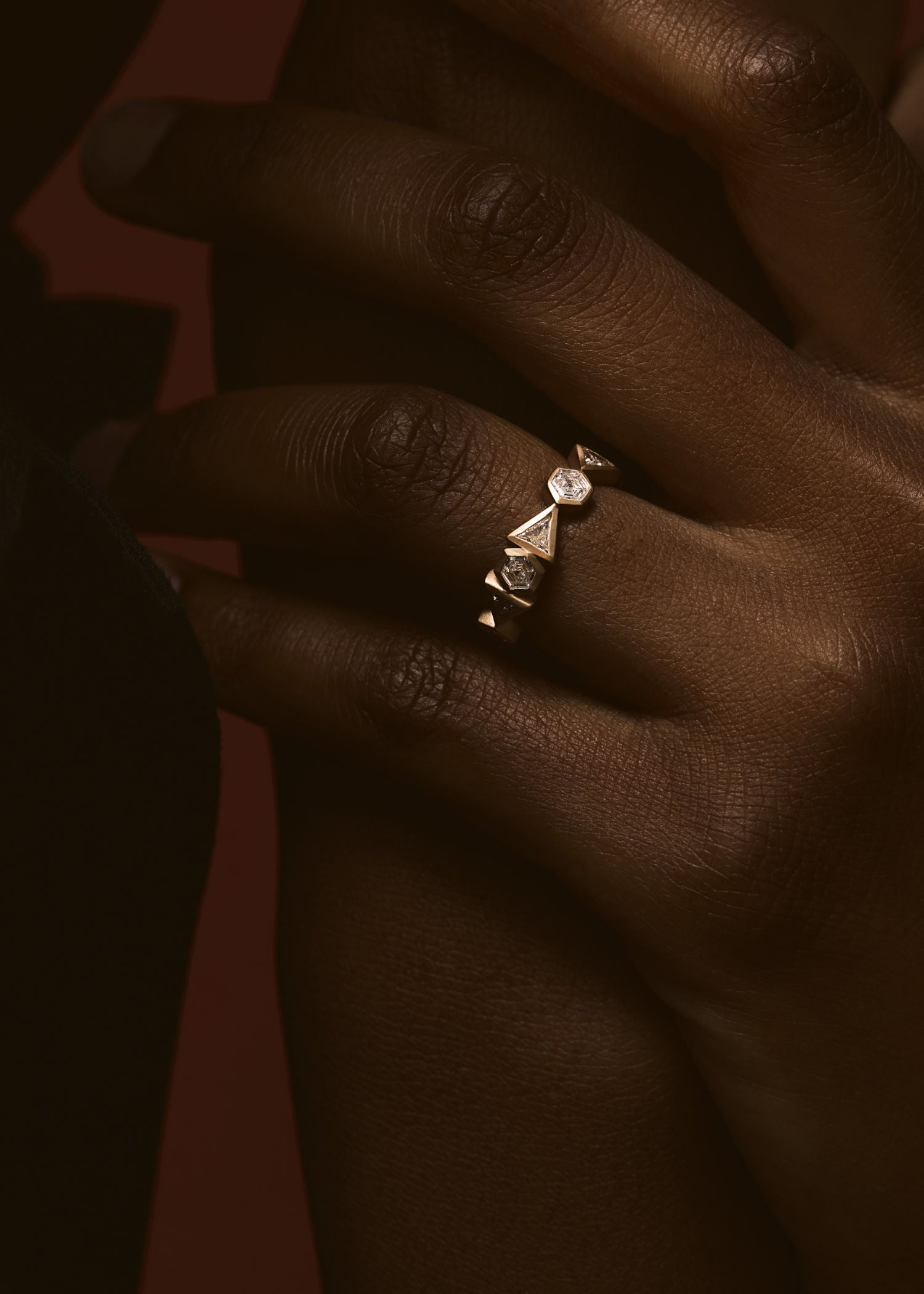 Model wearing gold diamond crown ring with geometric design on finger.