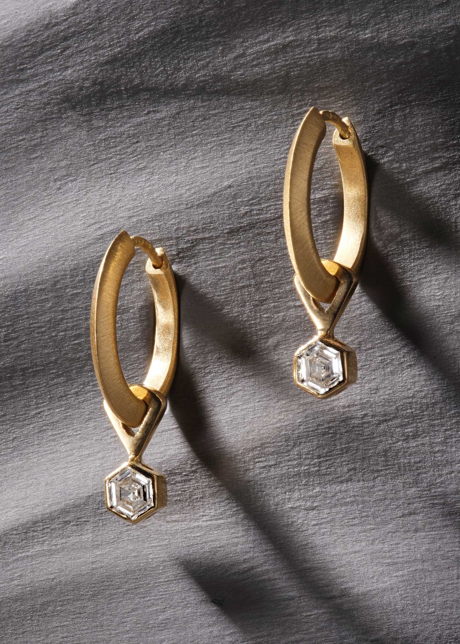 Yellow gold hoop earrings featuring hexagon-cut diamonds on grey textured surface.