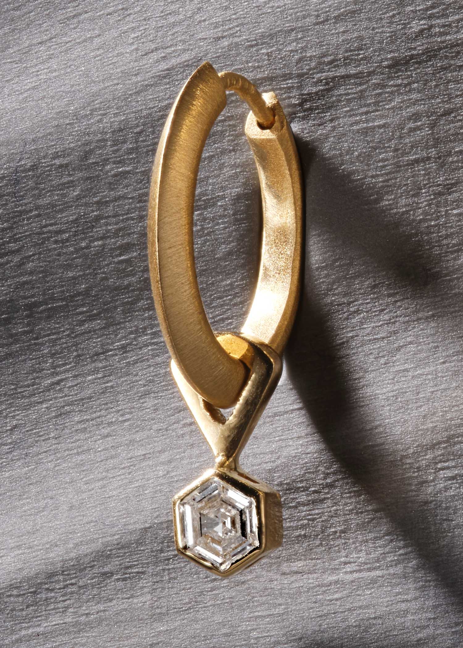 Close-up of yellow gold earring with hexagonal diamond in modern bezel setting.