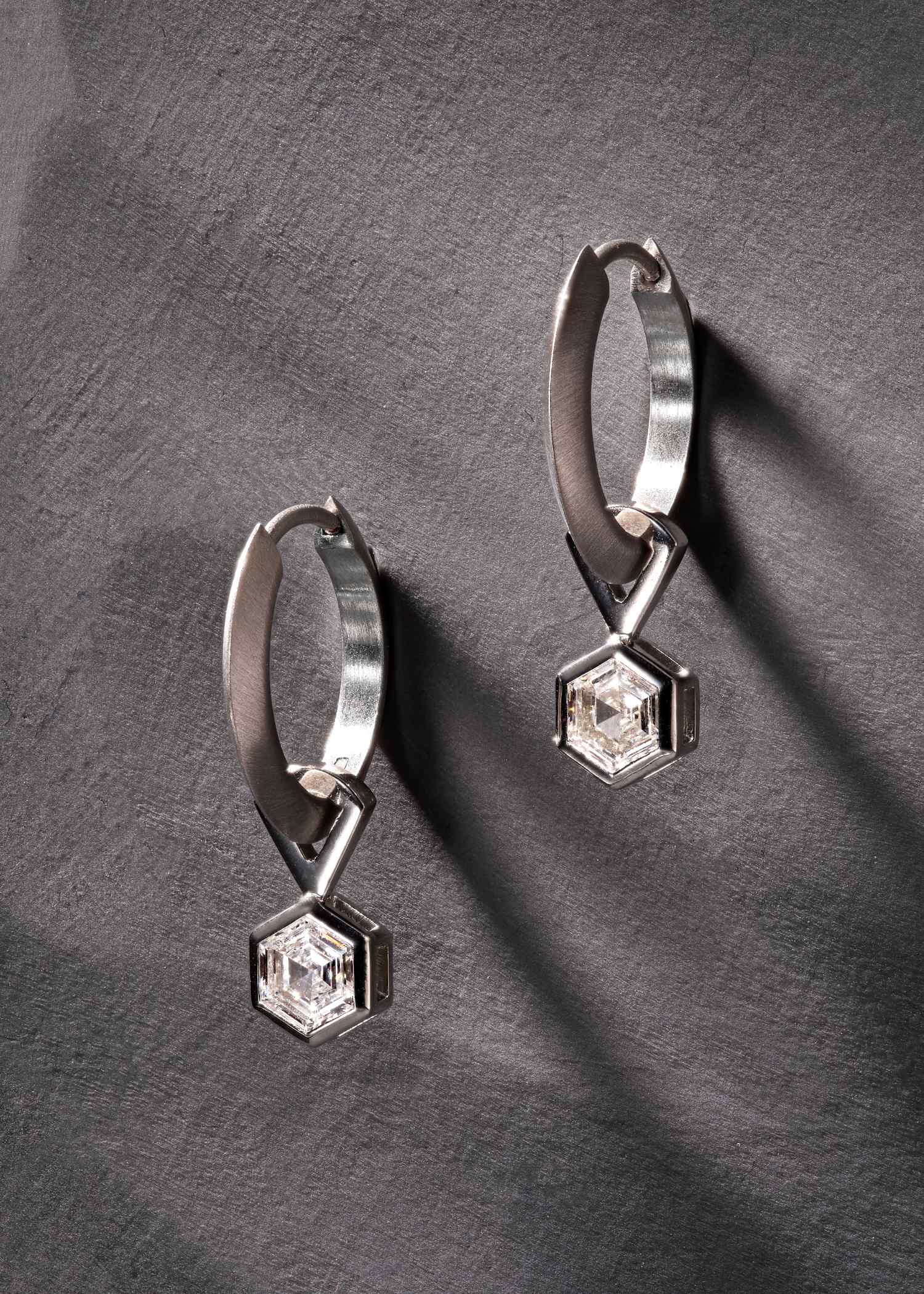 Platinum hoop earrings featuring hexagon-cut diamonds on grey textured surface.