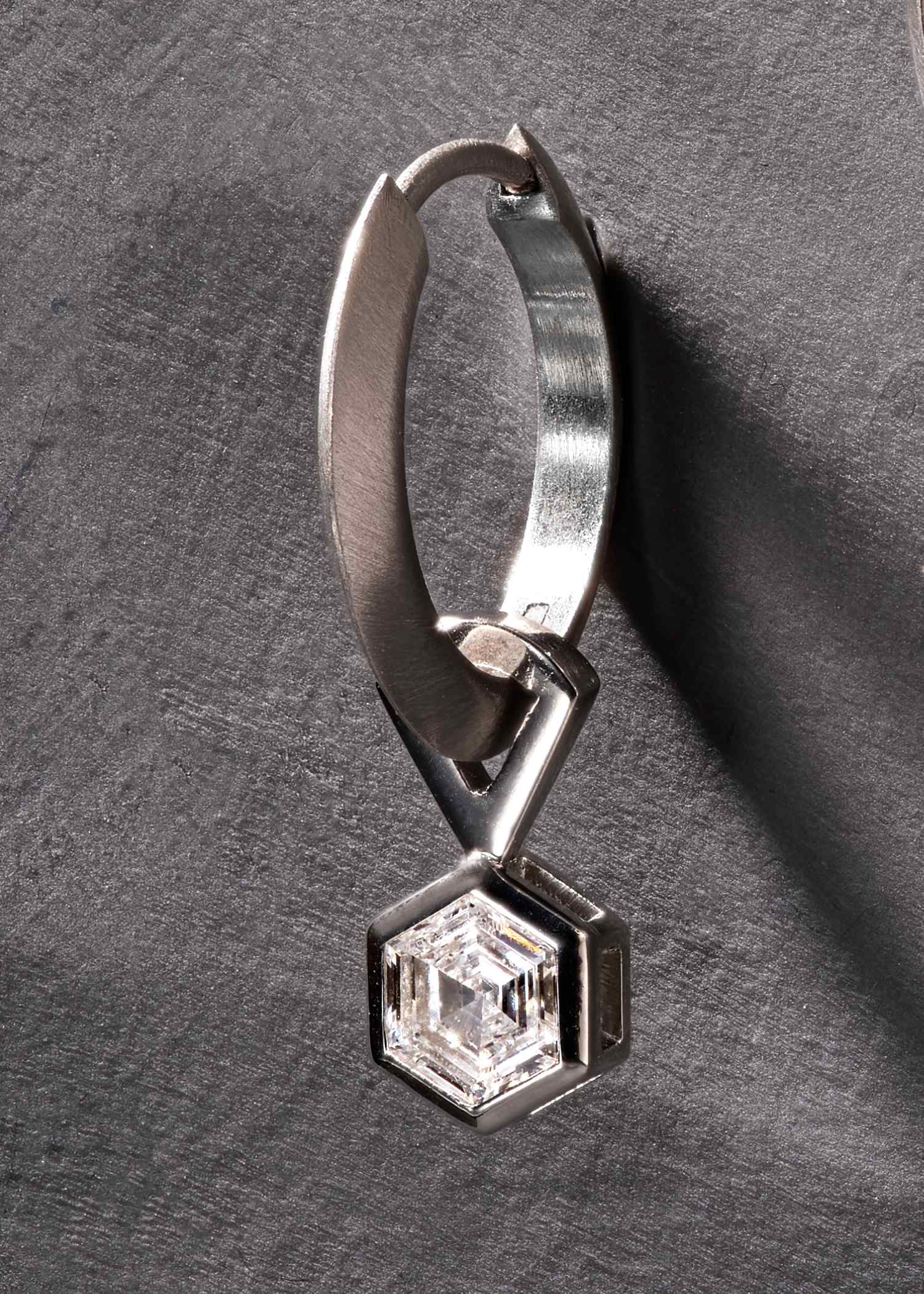Close-up of platinum hoop earring with hexagon-cut diamond in modern setting.
