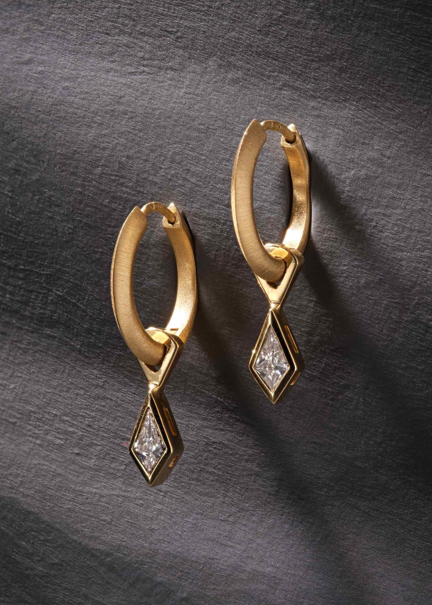 Yellow gold hoop earrings featuring kite-cut diamonds on dark textured surface.