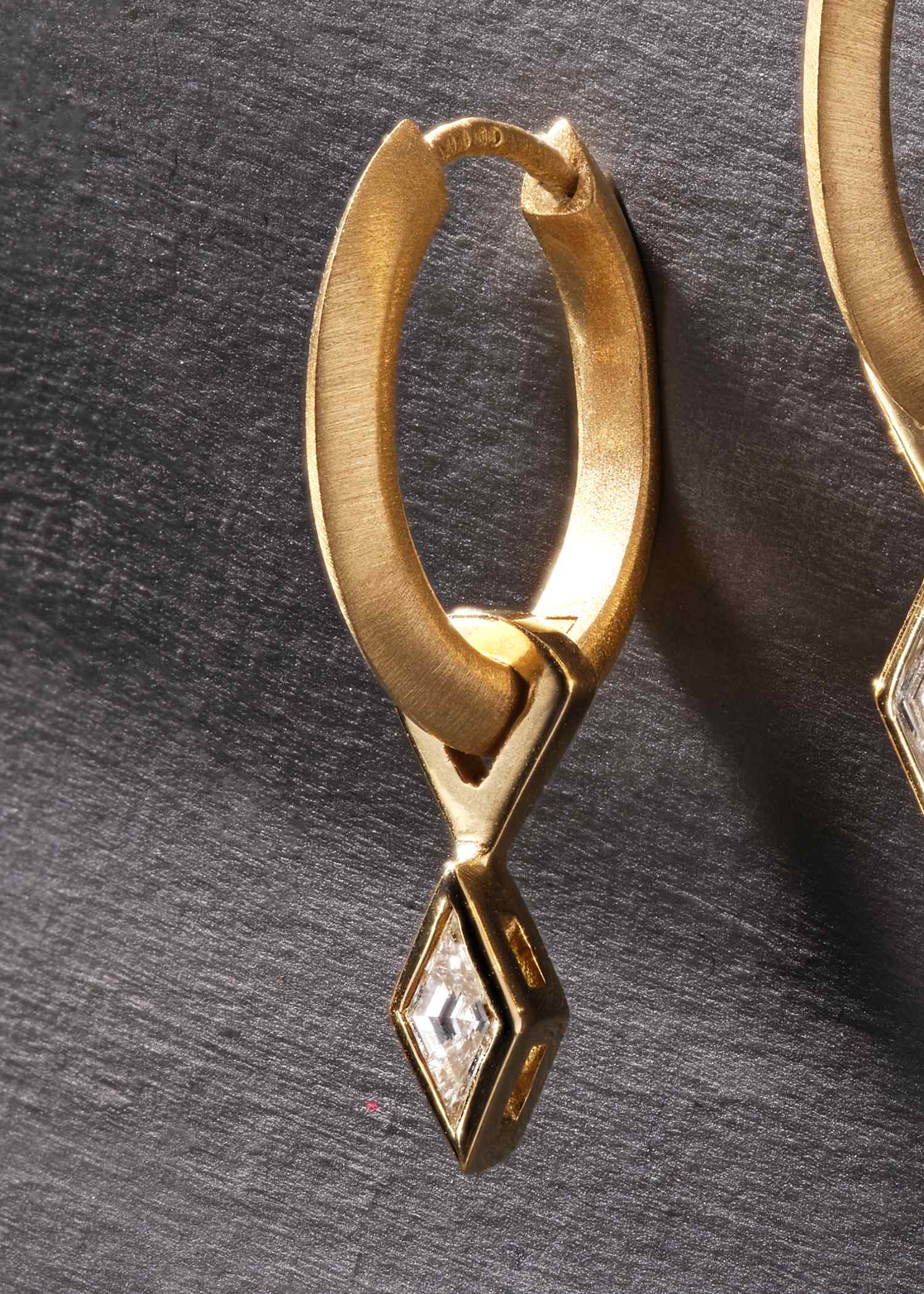 Detailed view of yellow gold earrings with lozenge-shaped diamonds in geometric setting.