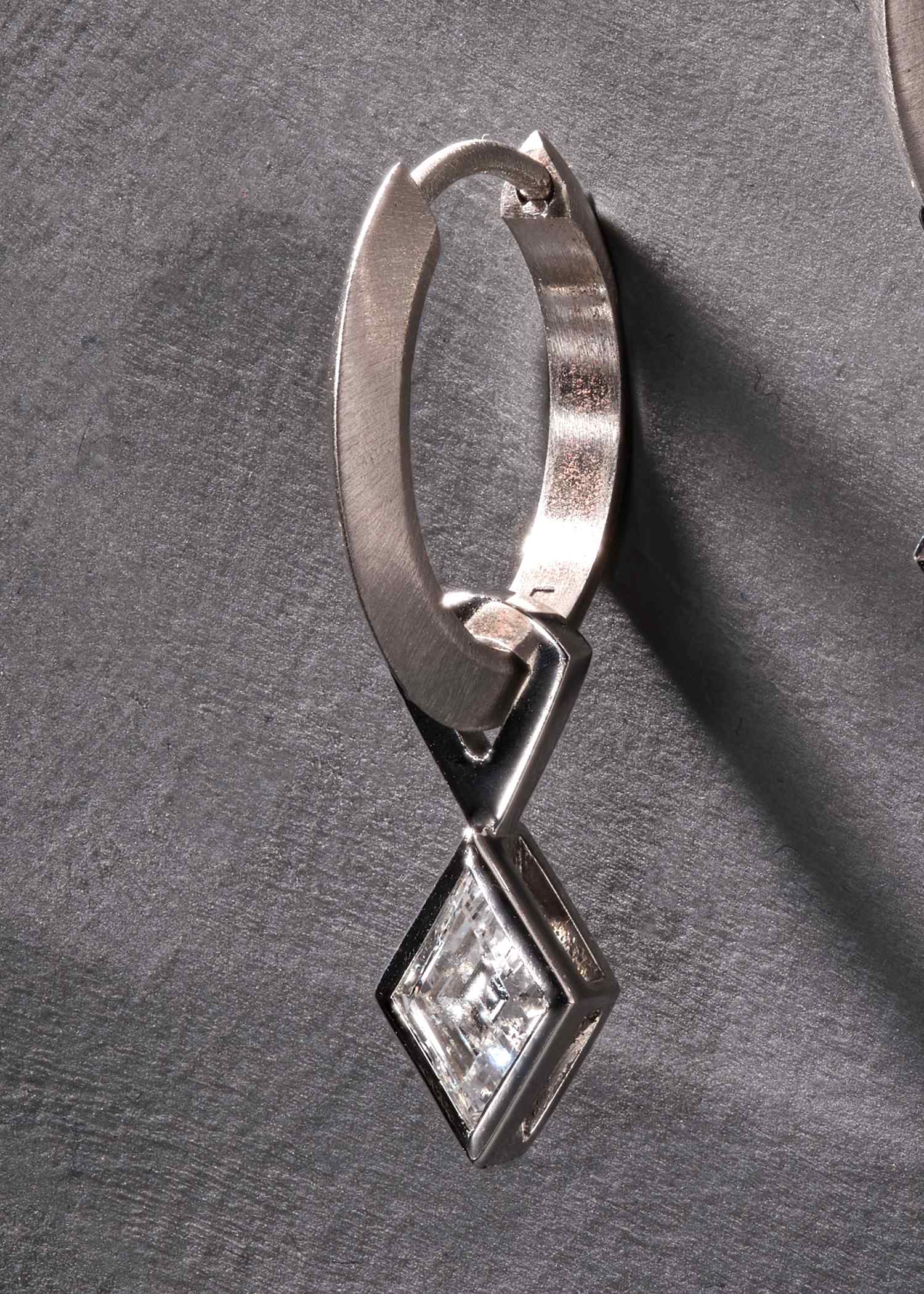 Close-up of platinum hoop earring with lozenge-cut diamond in sleek bezel setting.