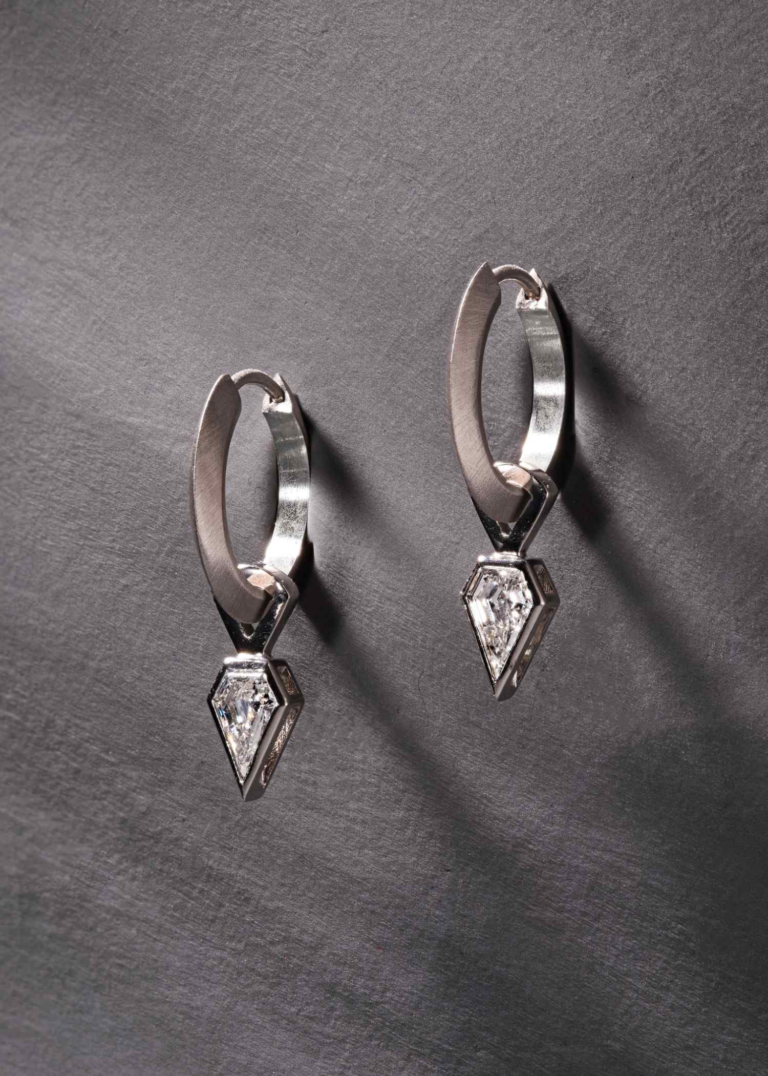 Platinum hoop earrings featuring shield-cut diamonds on grey textured background.