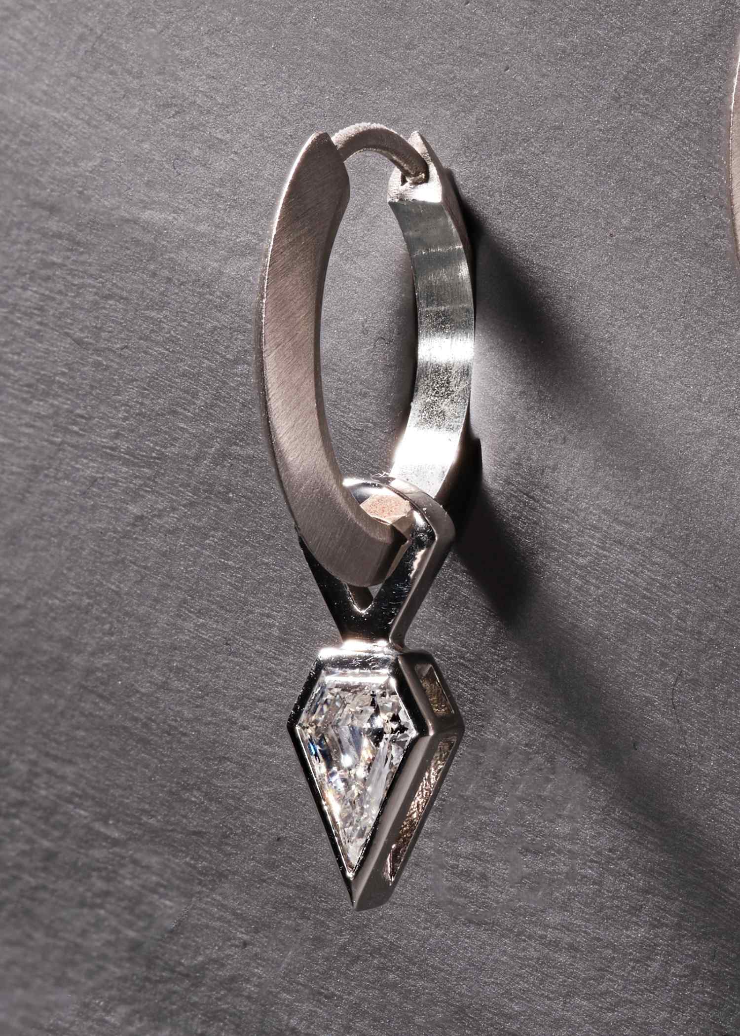 Close-up of platinum hoop earring with shield-cut diamond in modern geometric setting.