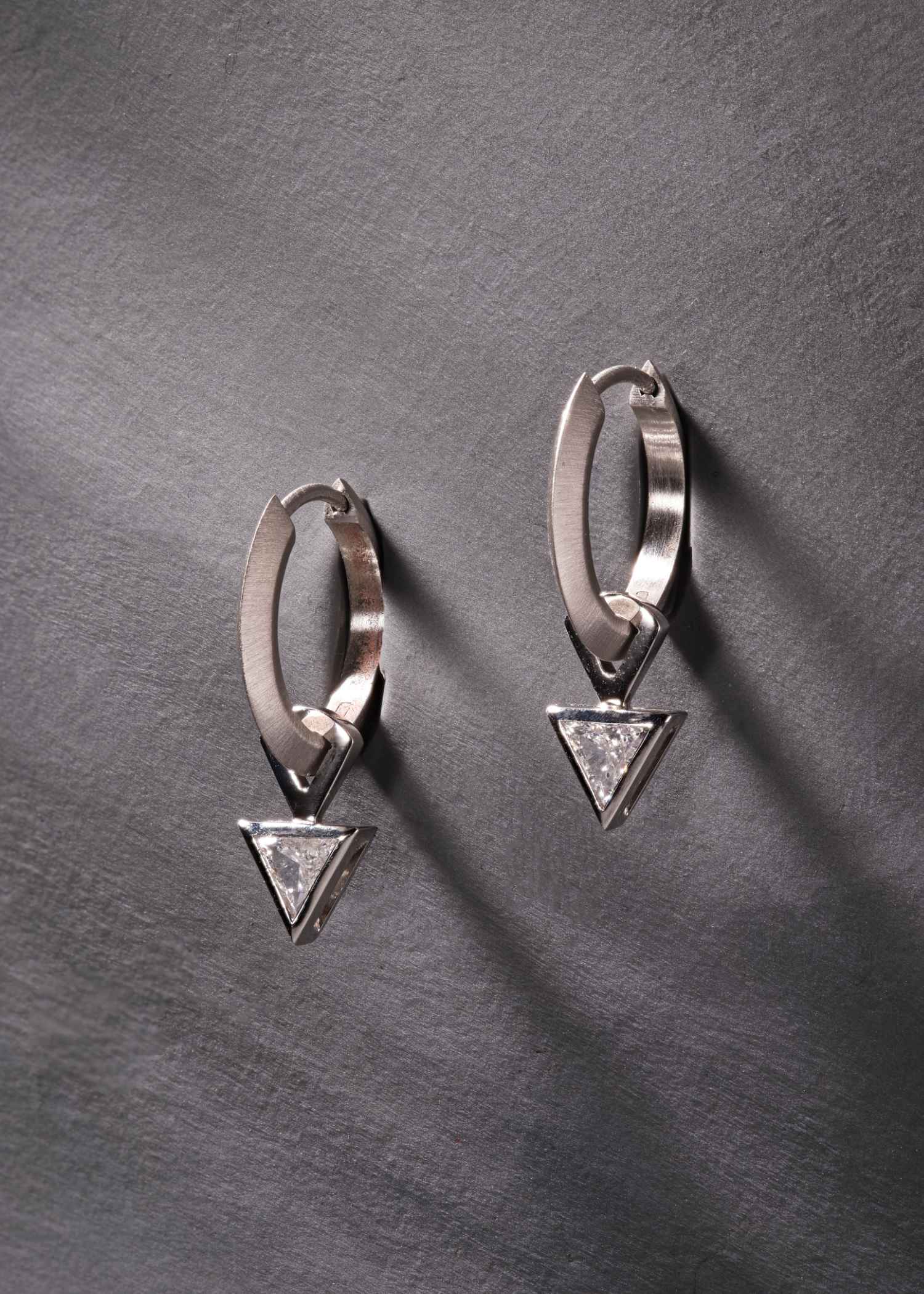 Platinum hoop earrings featuring triangular-cut diamonds on grey textured background.