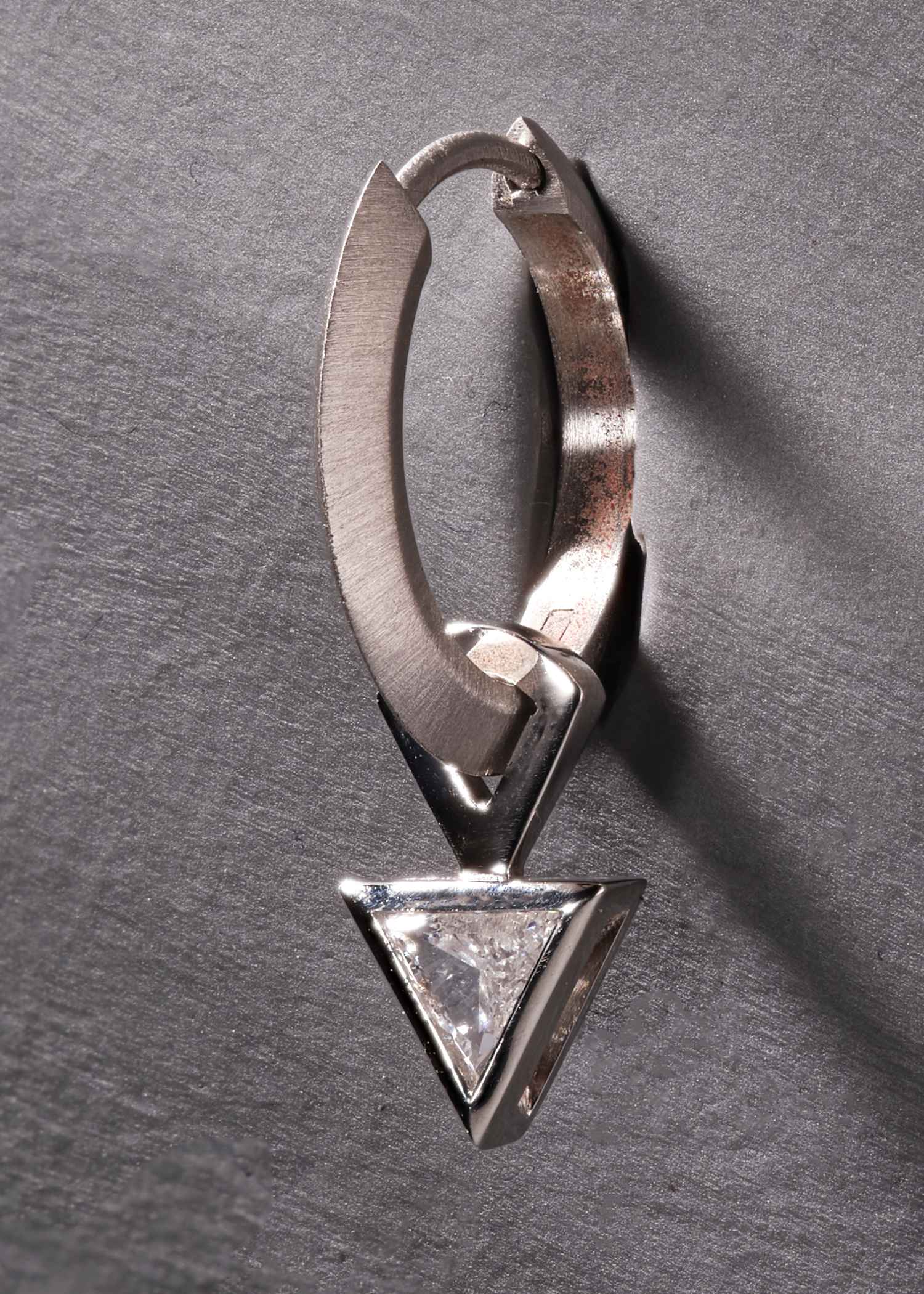 Close-up of platinum hoop earring with triangular-cut diamond in modern bezel setting.