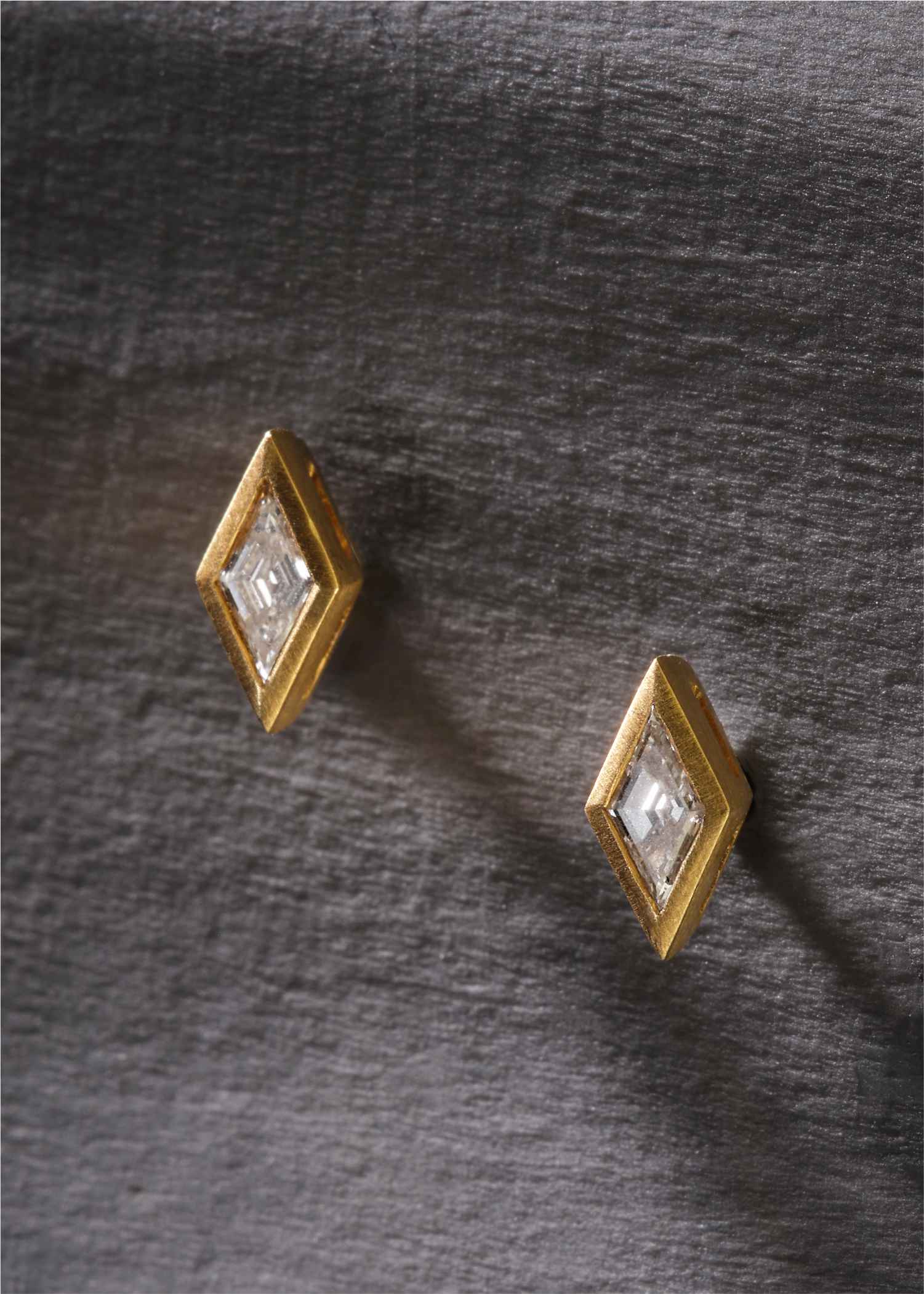 Pair of small hexagon-shaped gold stud earrings with clear gemstones, displayed on a white background.