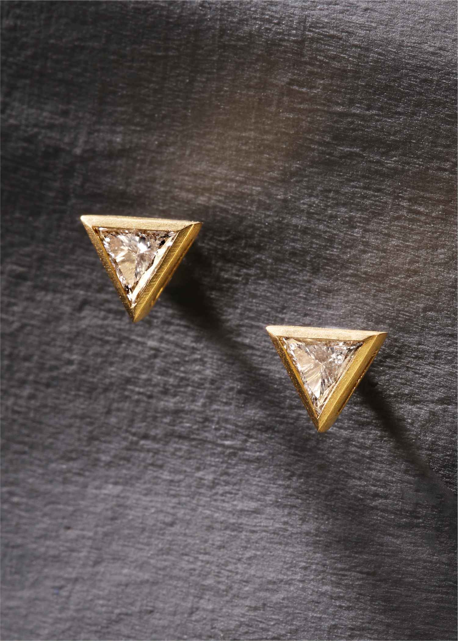 Pair of triangle-shaped earrings with clear gemstones on a light gray background.