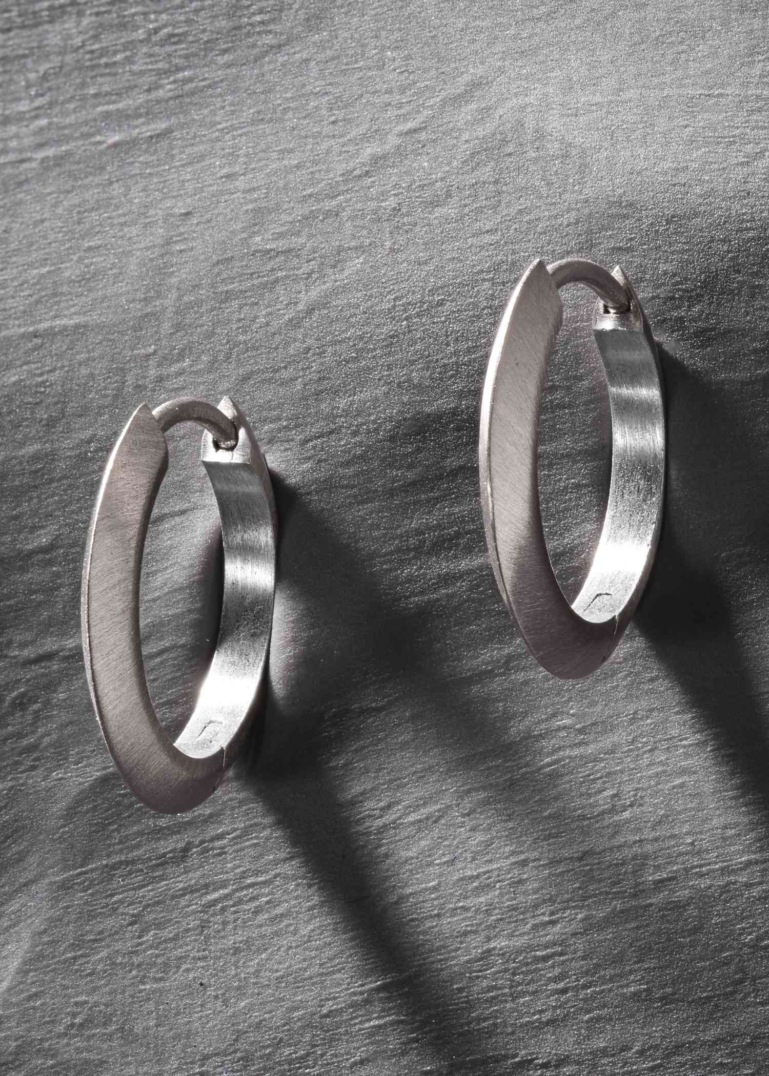 Brushed platinum oval hoop earrings with soft matte finish on grey background.