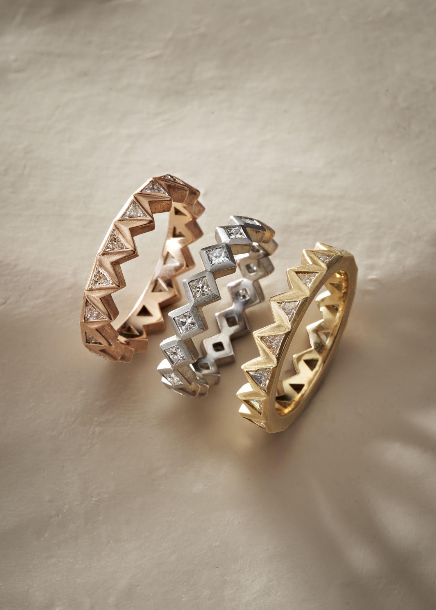 Two geometric rings, one in gold and one in silver, featuring zigzag patterns with embedded diamonds, displayed on a white background.