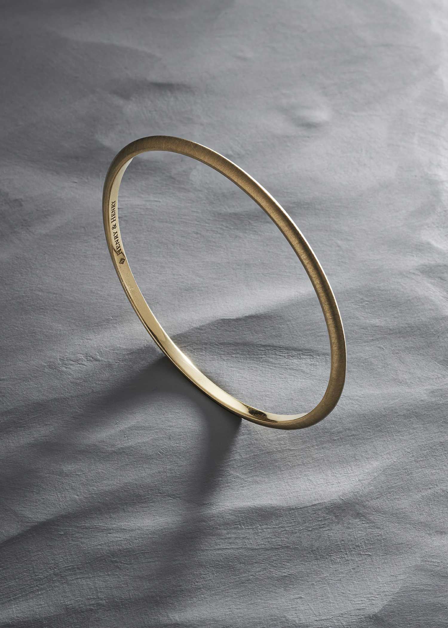 Yellow gold bracelet on a textured gray surface.