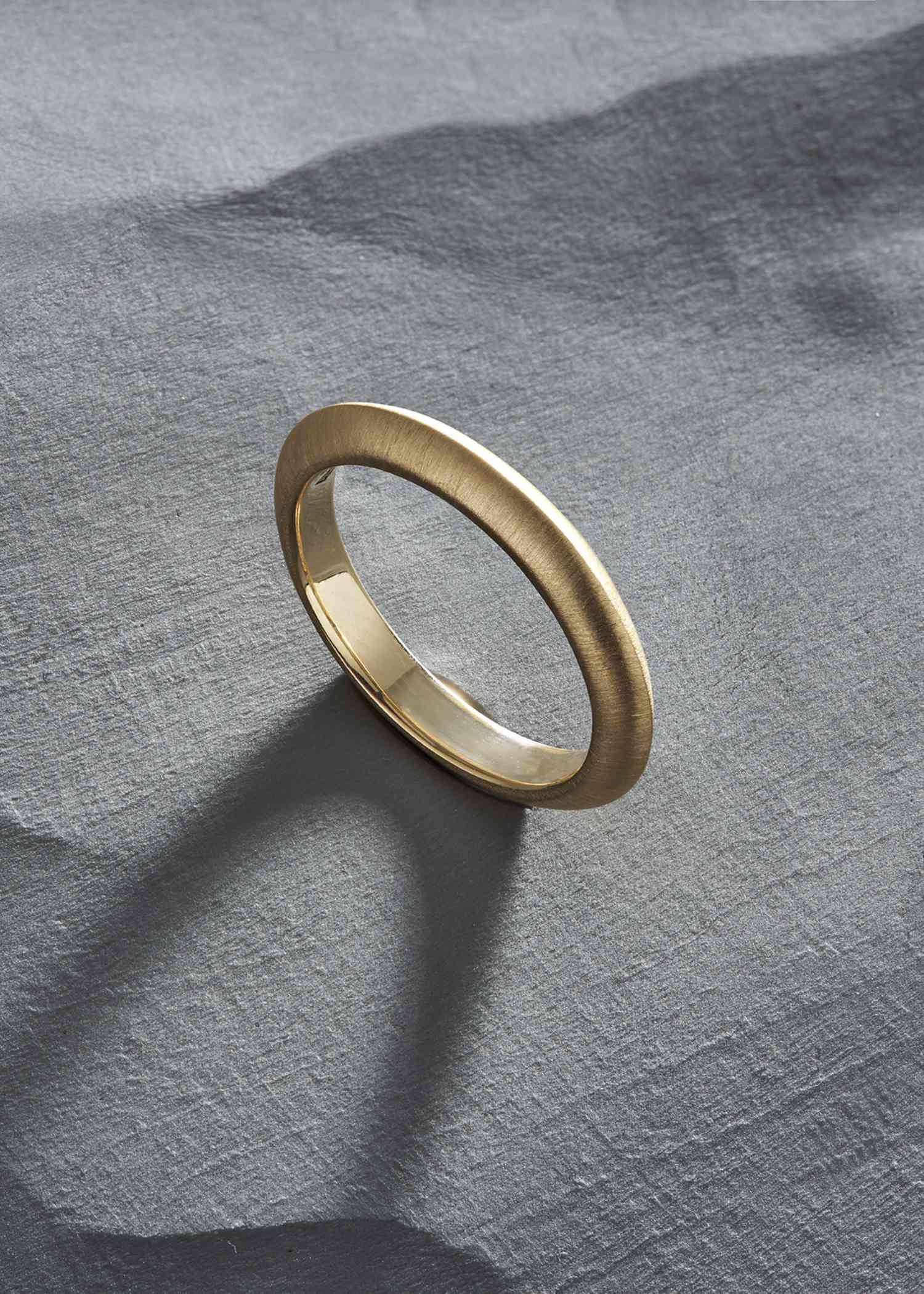 Simple yellow gold knife-edge ring on a textured gray surface.