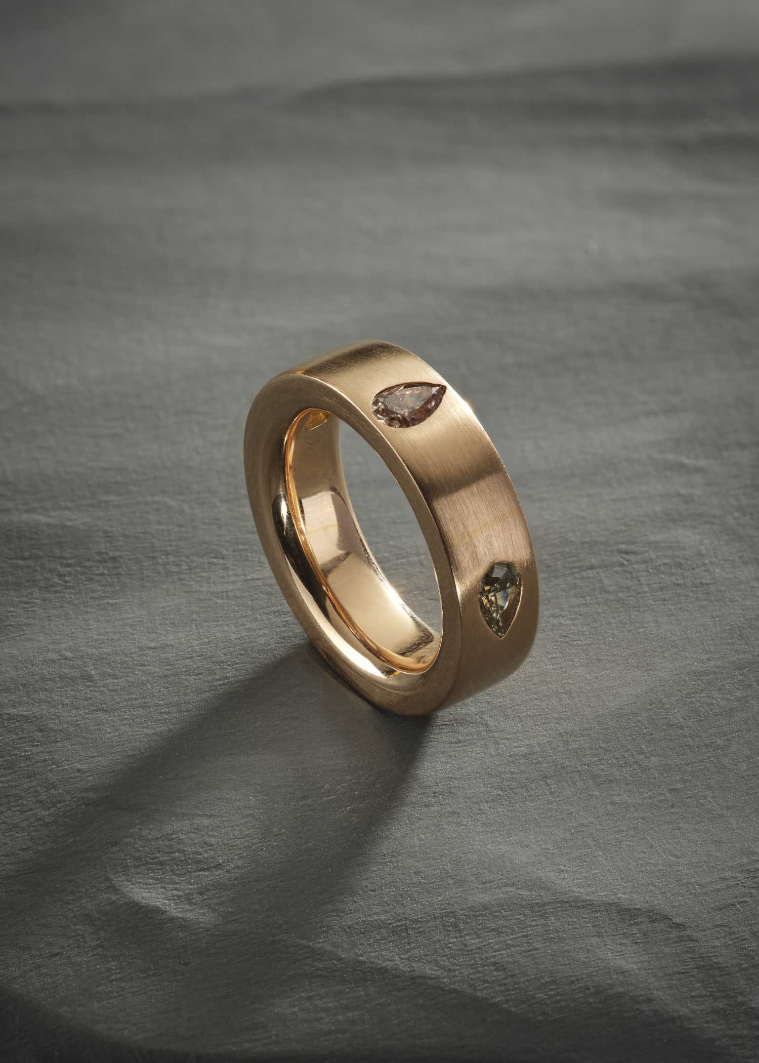 Rose gold ring with pear-cut diamonds on matte textured surface.