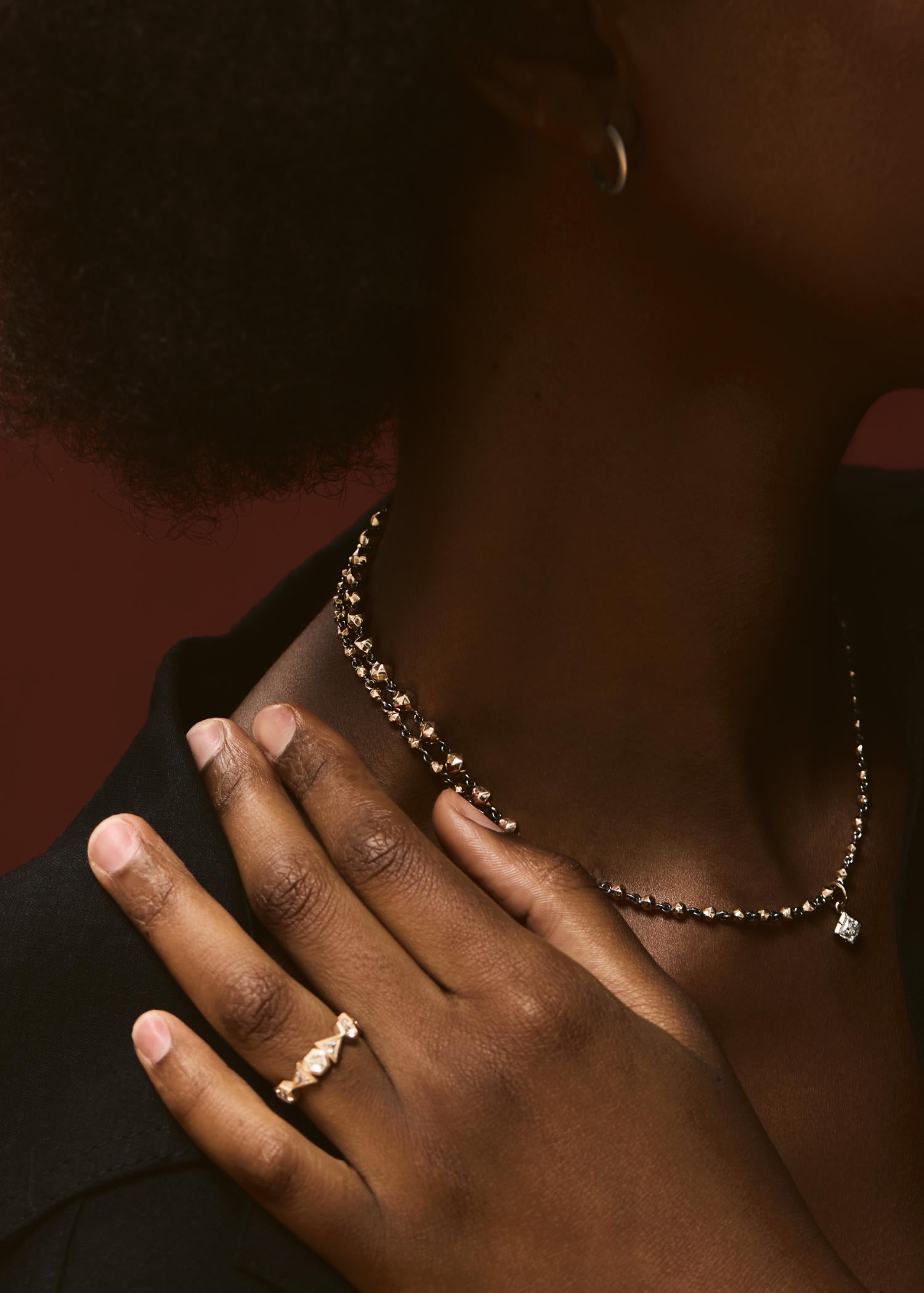 Close-up of a person wearing a necklace and ring with a dark background.