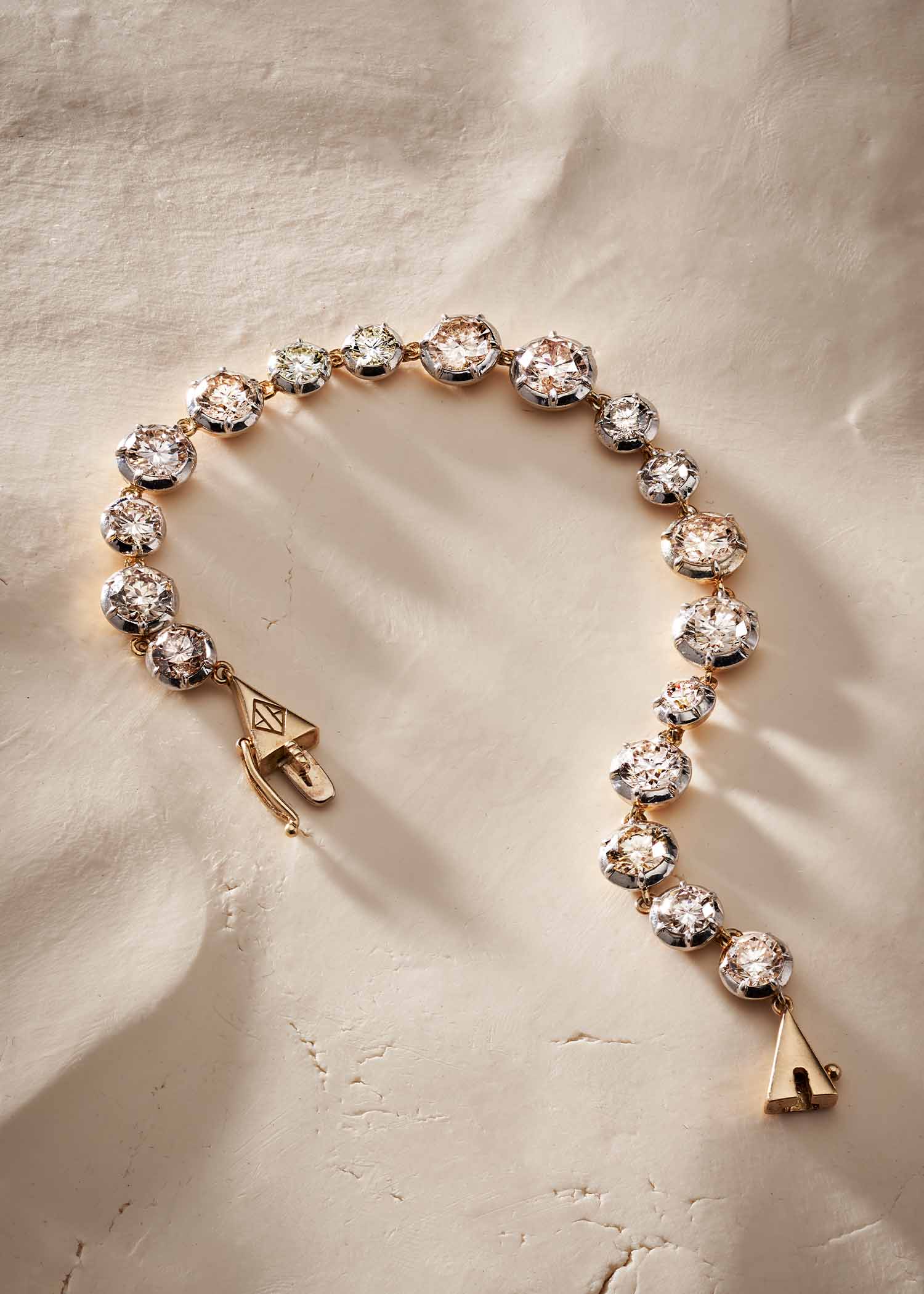 Gold diamond tennis bracelet with round-cut diamonds displayed on a soft beige textured surface.