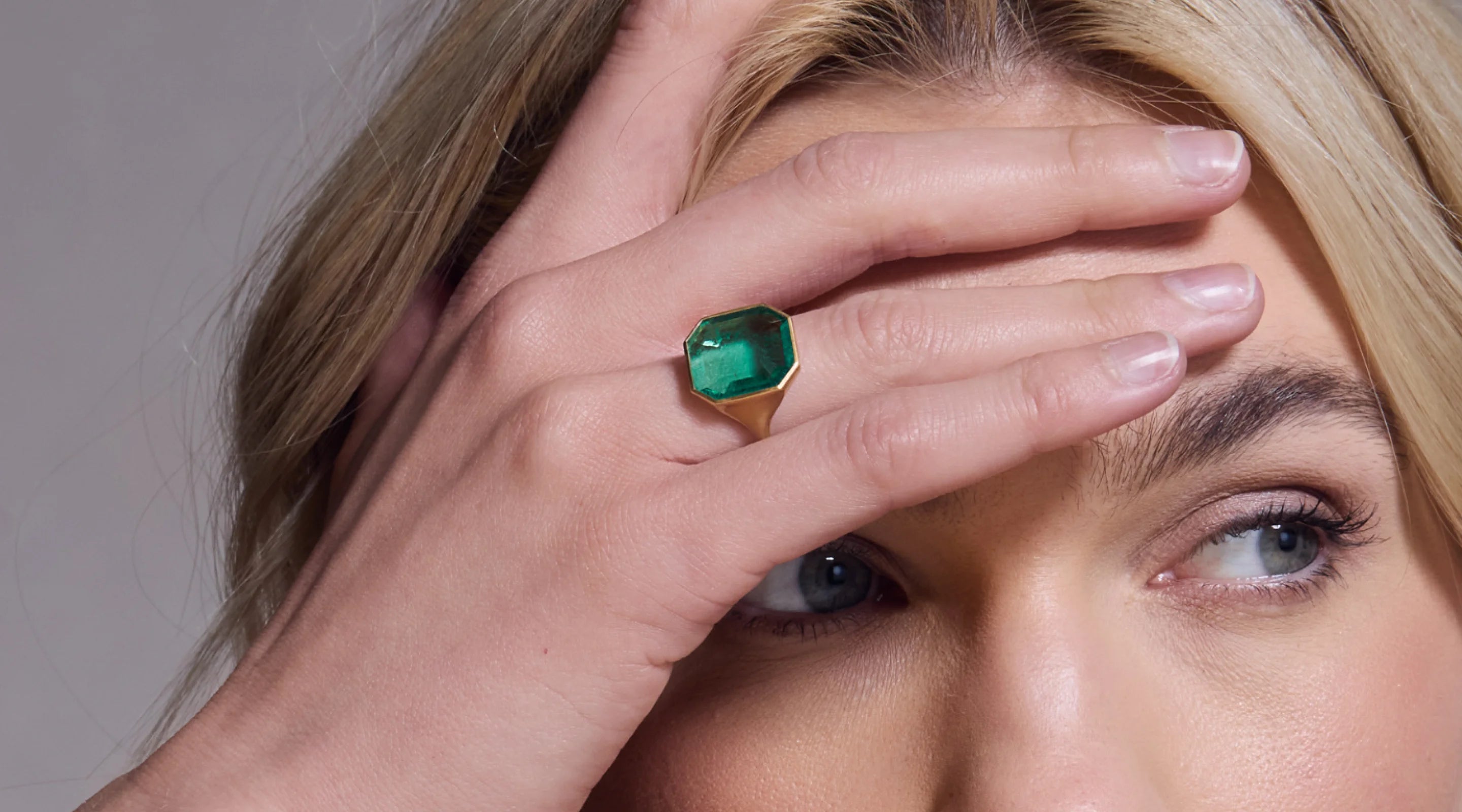 Blonde woman with slicked-back hair wearing a black strapless top and a choker necklace with a large light blue gemstone.