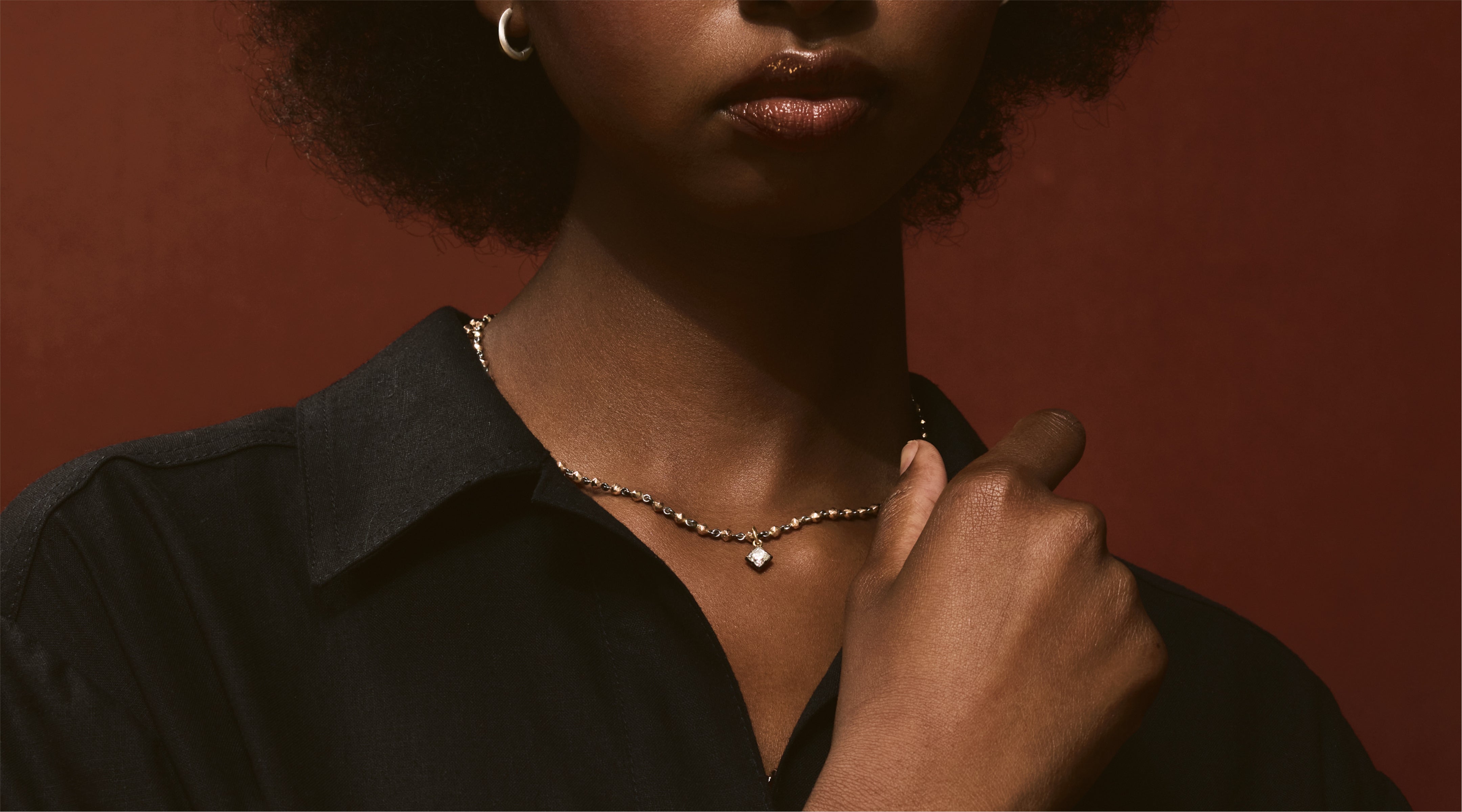 Blonde woman with slicked-back hair wearing a black strapless top and a choker necklace with a large light blue gemstone.