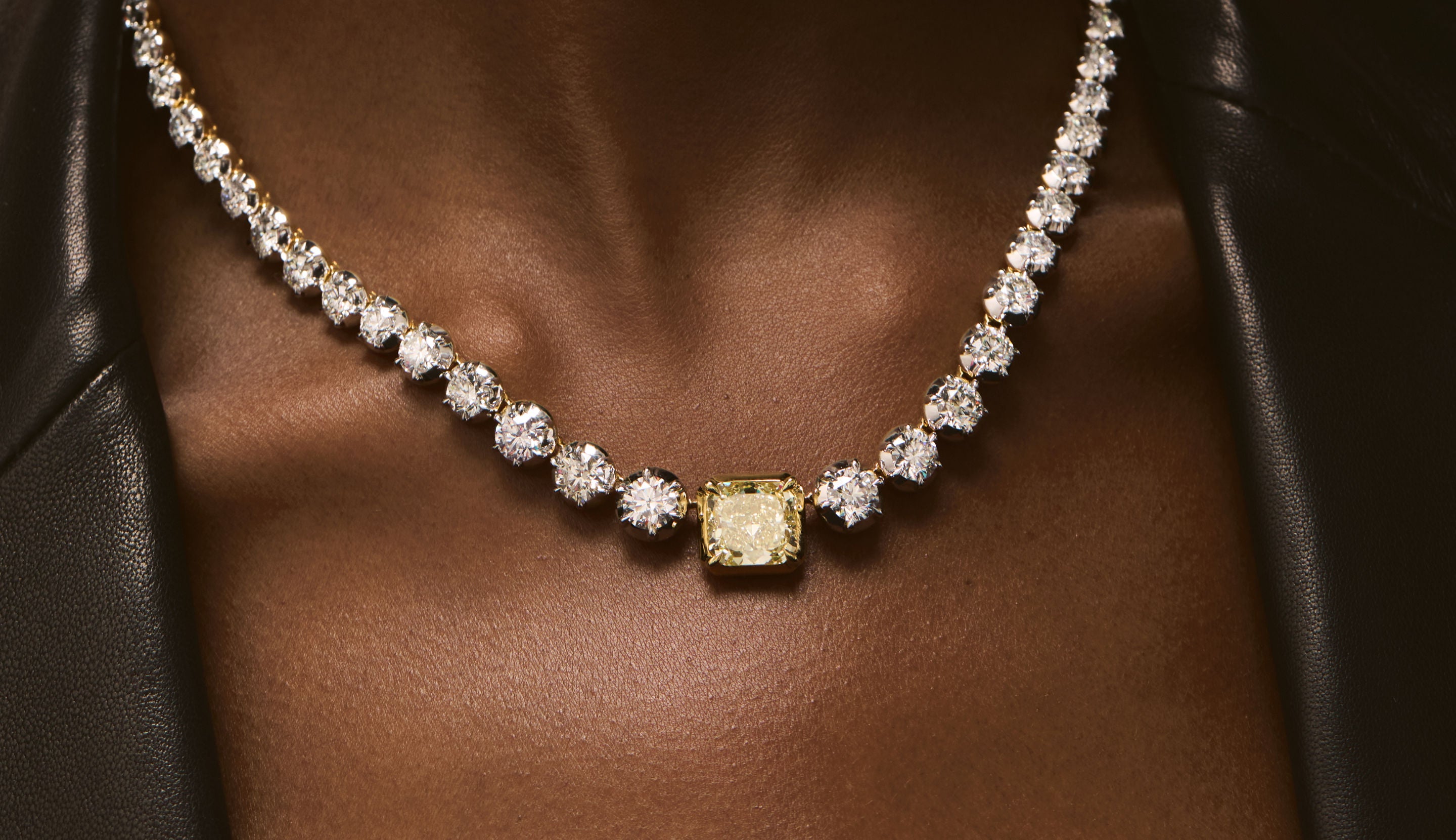 Blonde woman with slicked-back hair wearing a black strapless top and a choker necklace with a large light blue gemstone.