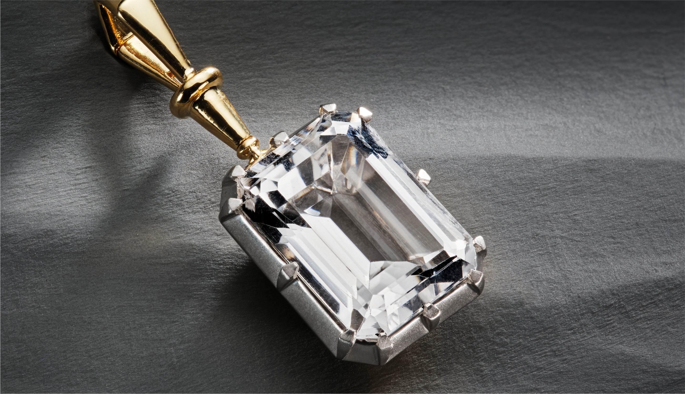 Blonde woman with slicked-back hair wearing a black strapless top and a choker necklace with a large light blue gemstone.