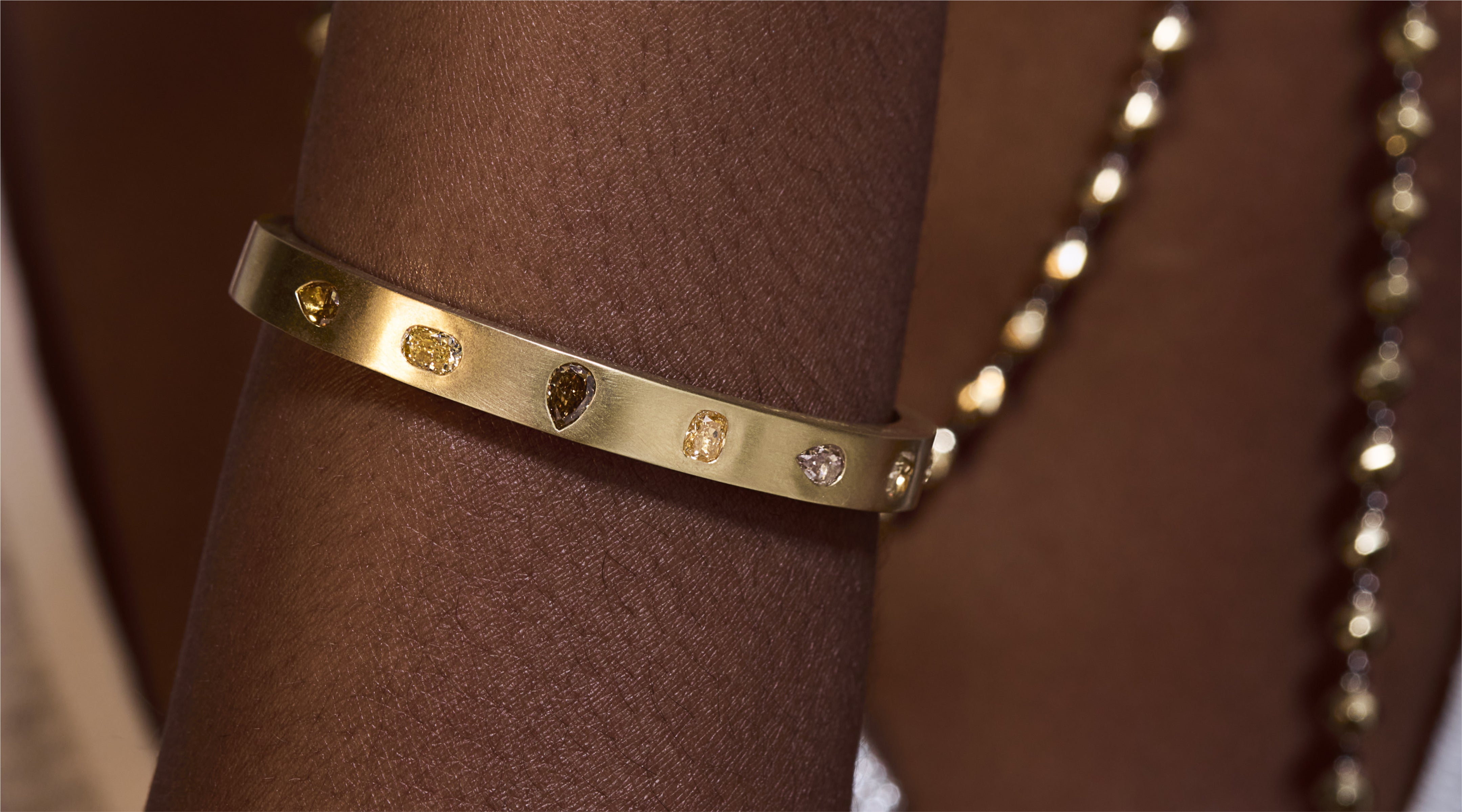Blonde woman with slicked-back hair wearing a black strapless top and a choker necklace with a large light blue gemstone.