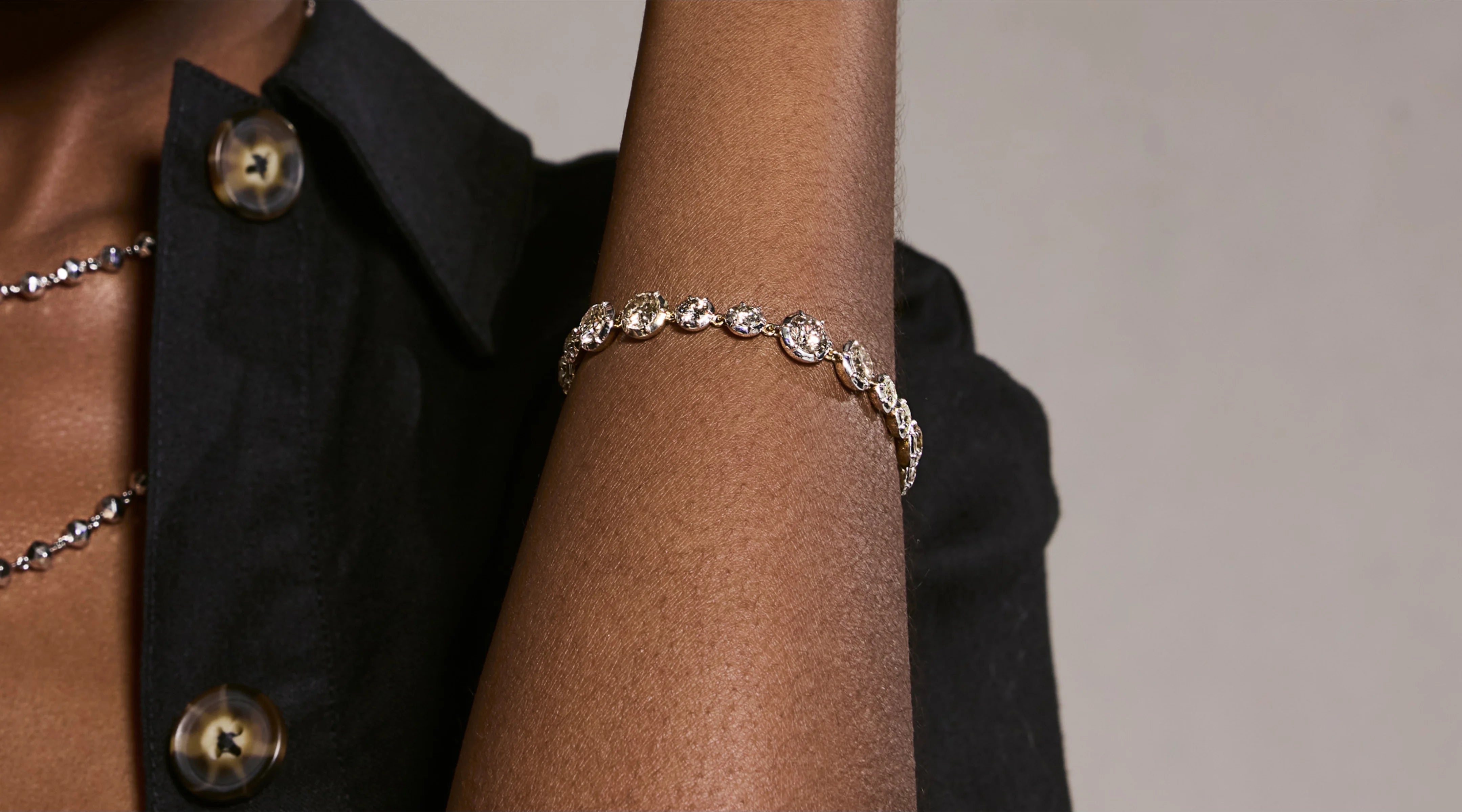 Blonde woman with slicked-back hair wearing a black strapless top and a choker necklace with a large light blue gemstone.