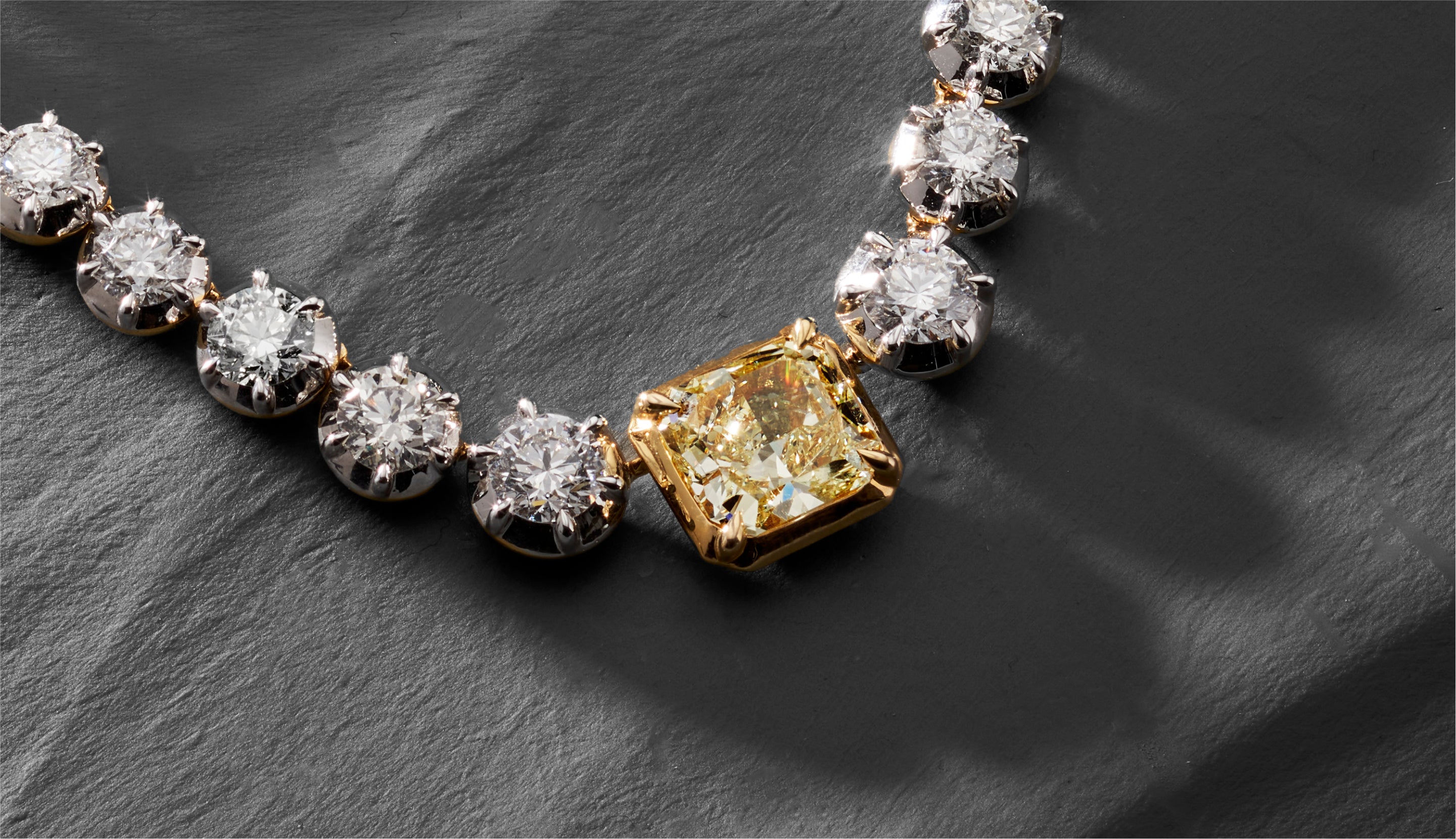 Blonde woman with slicked-back hair wearing a black strapless top and a choker necklace with a large light blue gemstone.